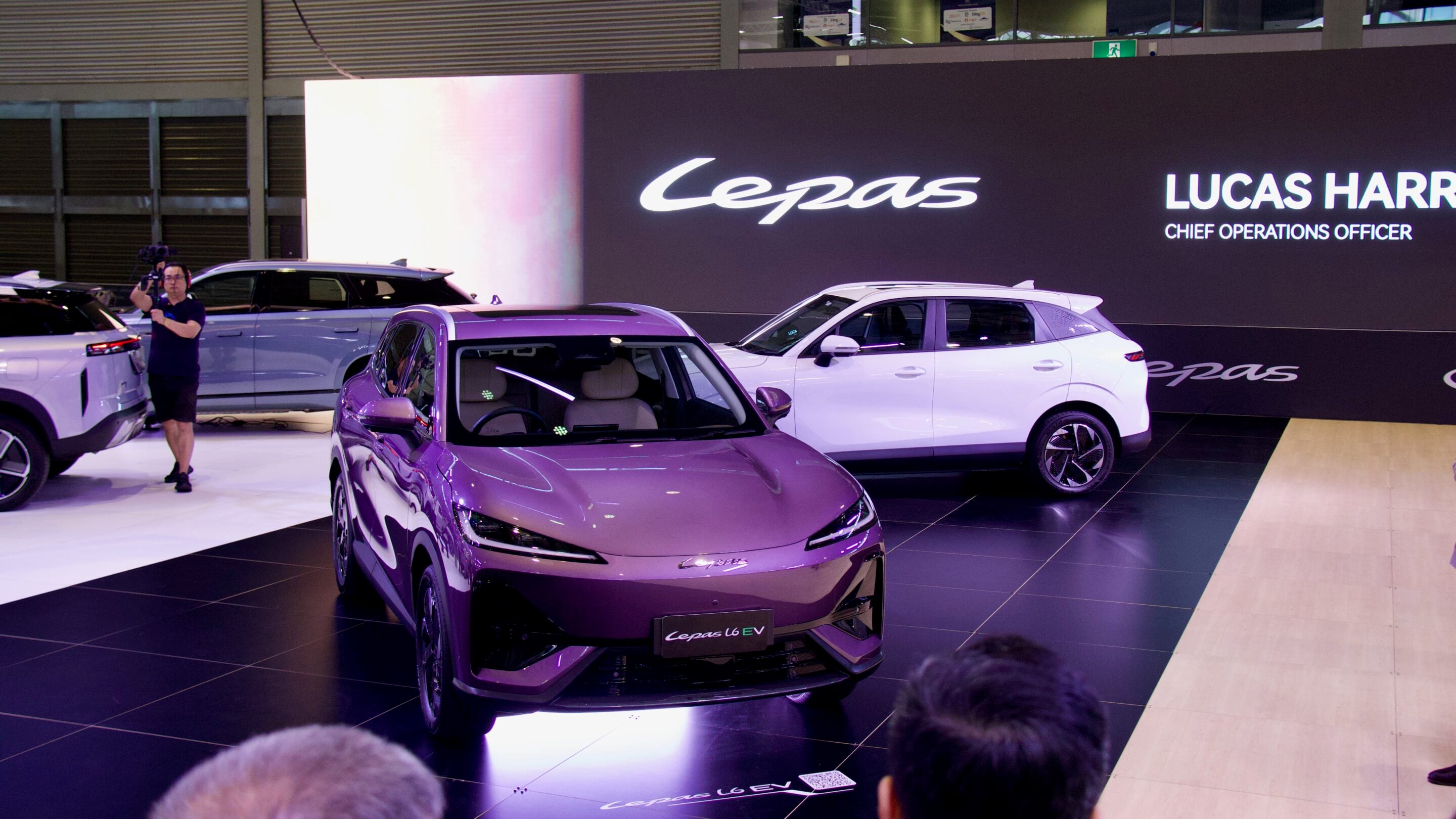 Purple Lépas L6 EV on a showroom floor with other cars and a large 'Lepas' sign in the background.