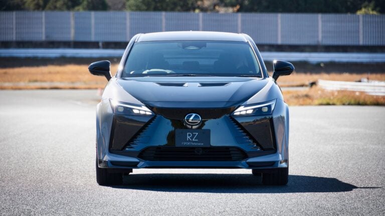 Front view of a silver Lexus RZ electric SUV facing the camera on a sunlit racetrack/parking area.
