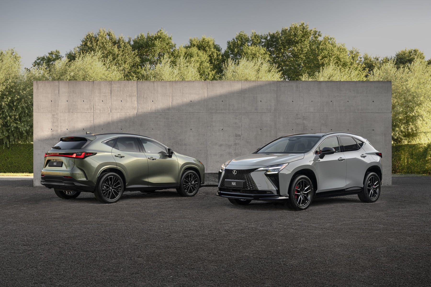 Two Lexus NX SUVs parked side by side in a lot, green on the left and silver on the right, with a concrete wall and trees behind.”, “Green and silver Lexus NX crossovers parked parallel in front of a tall concrete barrier.”, “A green Lexus NX and a silver Lexus NX in a parking area, with a concrete wall and greenery in the background.”, “Two luxury crossover SUVs (Lexus NX) displayed in a lot beside a gray concrete wall.”, “Silver Lexus NX (front) and green Lexus NX (rear) parked next to a concrete barrier with trees in the backdrop.”]} }{}{