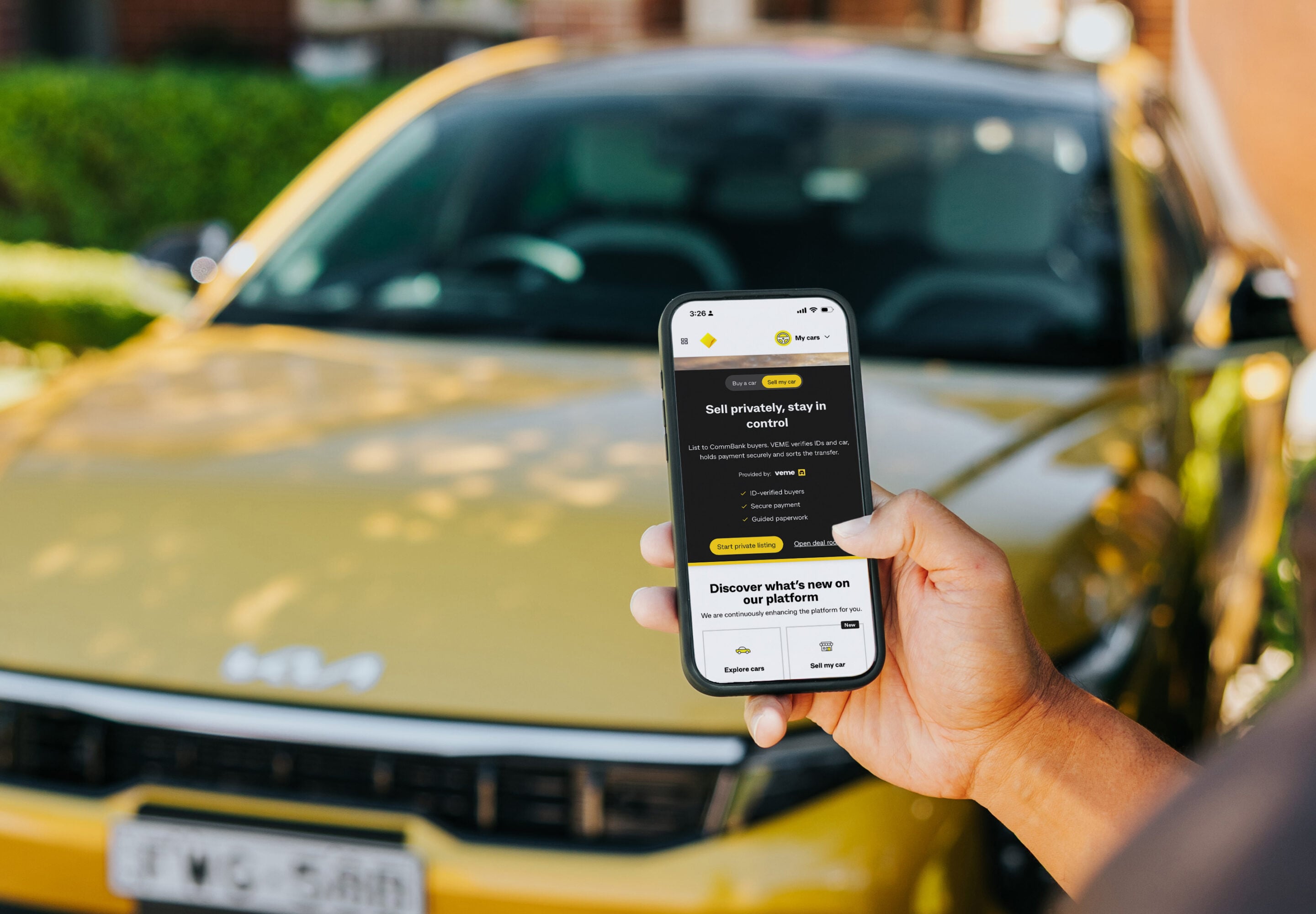 Person holding a smartphone showing a car-selling app in front of a yellow car, indicating online car listing.