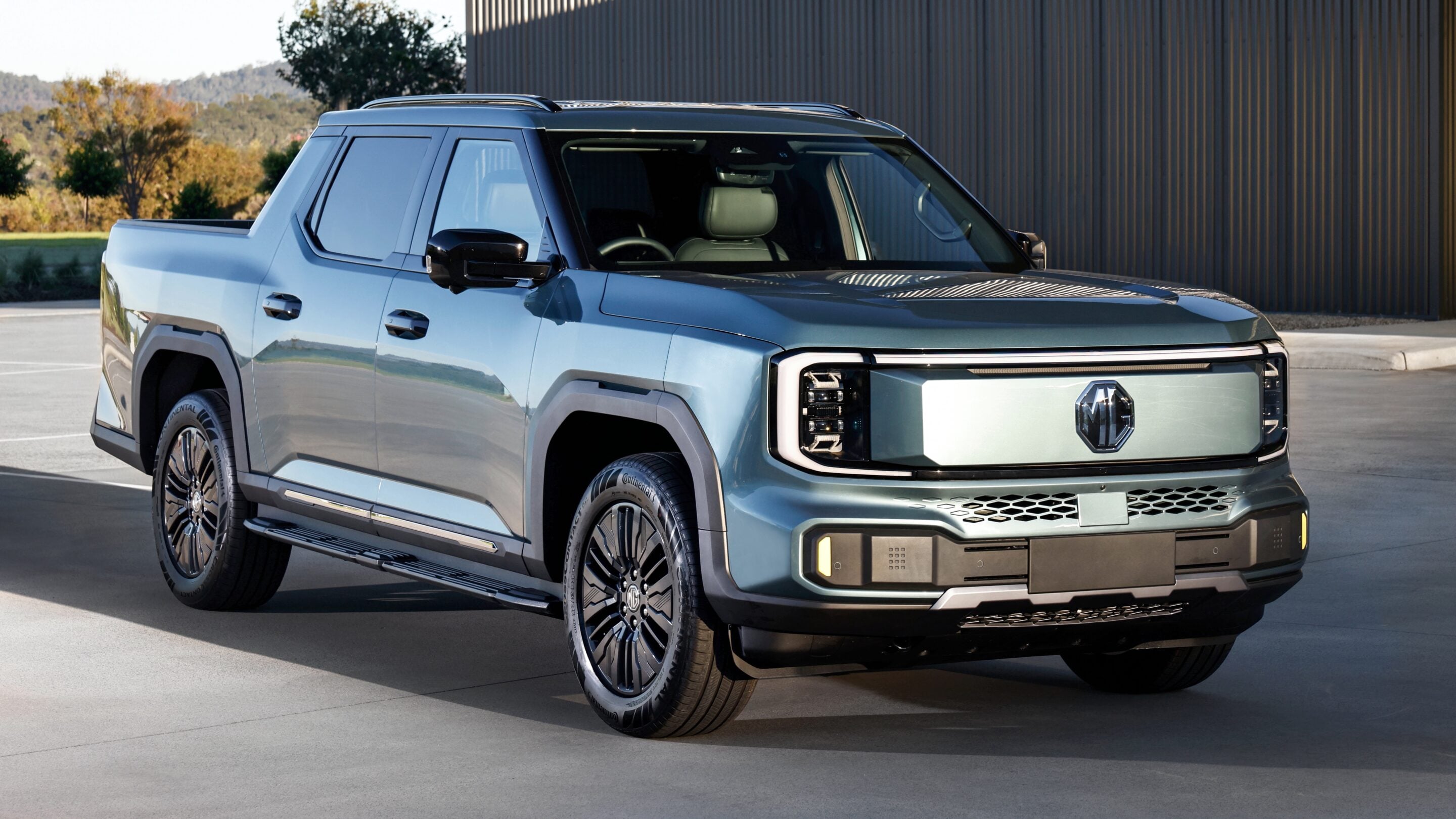 Blue pickup-style SUV shown from the front-right, parked on pavement with a dark corrugated wall in the background.