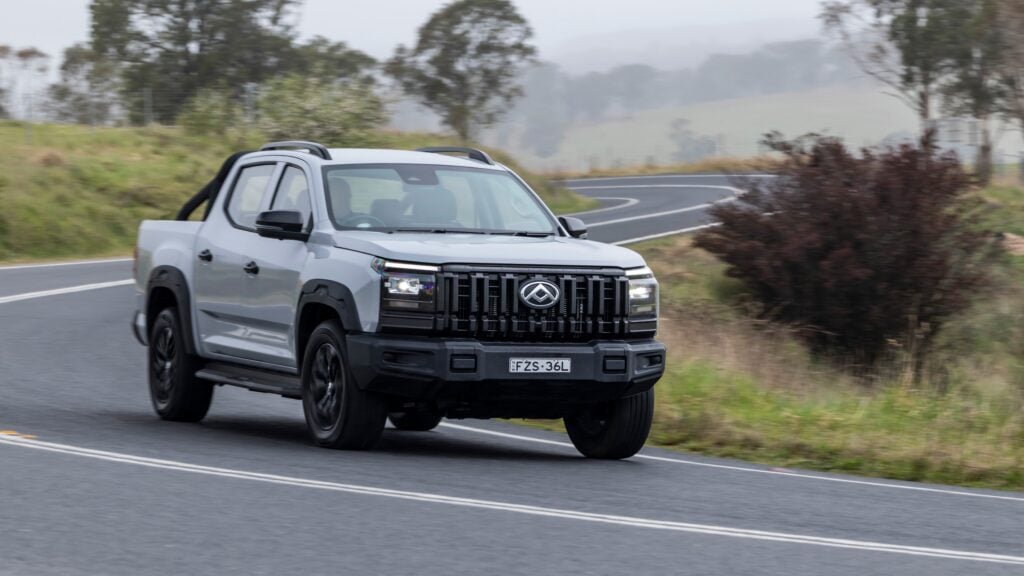 Silver pickup truck driving on a winding rural road, front view, mid-motion blur suggesting speed.