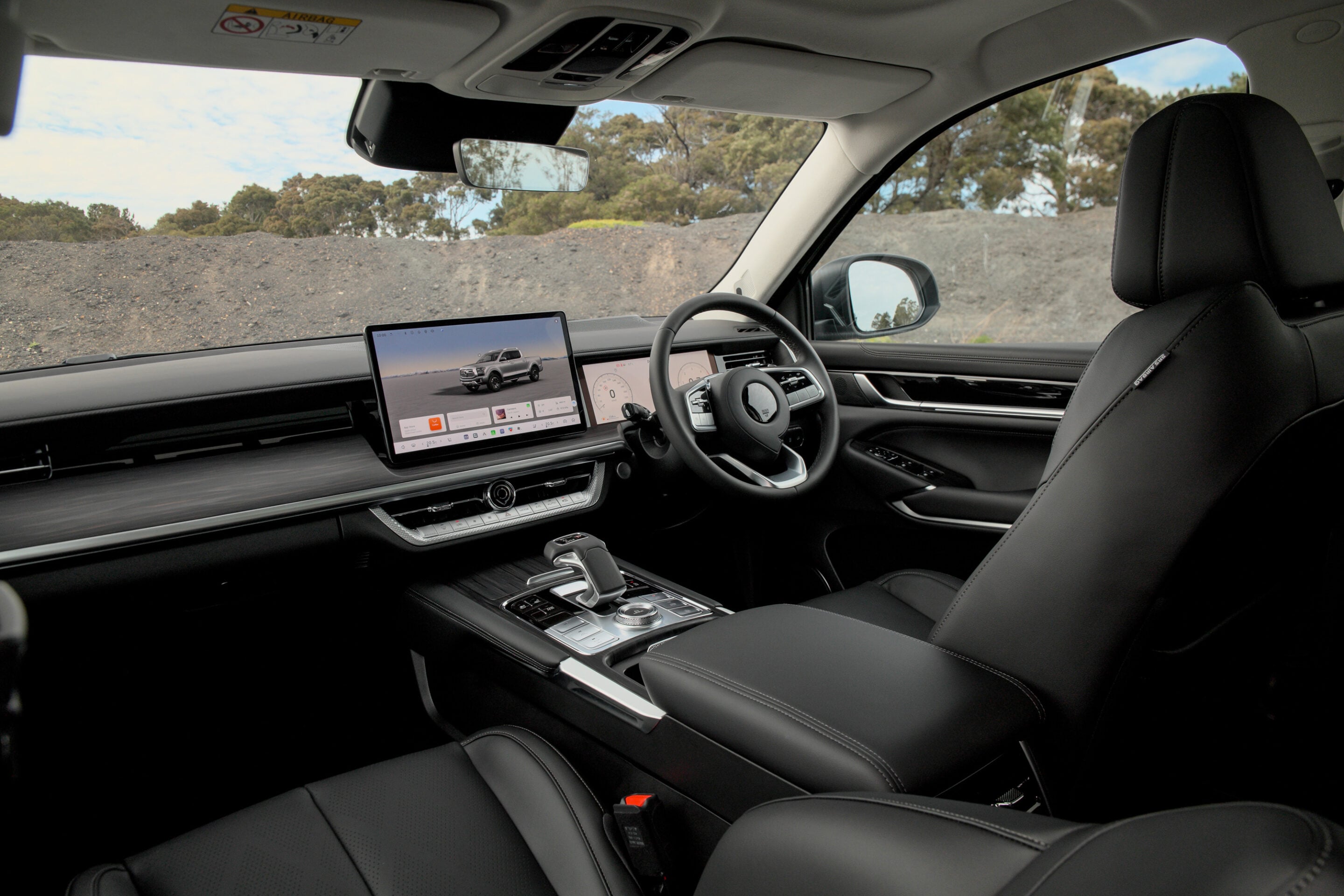 Modern car interior with a large central touchscreen display, steering wheel, and black leather seats in a dark cabin.