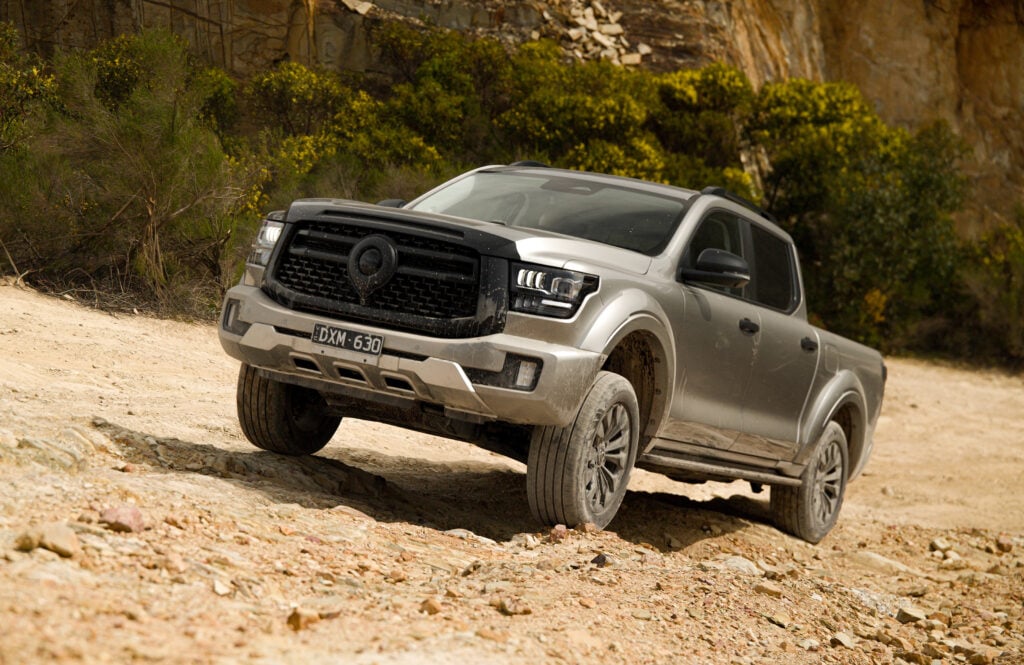Gray off-road pickup on a rocky dirt trail with a steep hillside and green shrubs in the background.