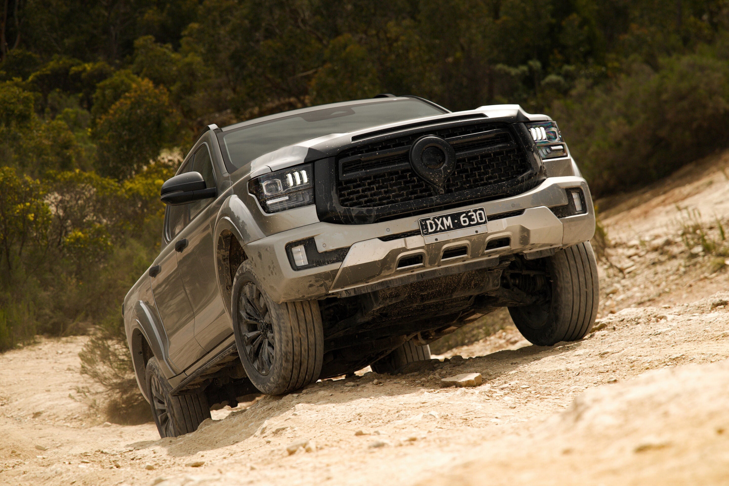 Off-road pickup truck on a steep dirt slope, kicking up dust with muddy tires and a forested background