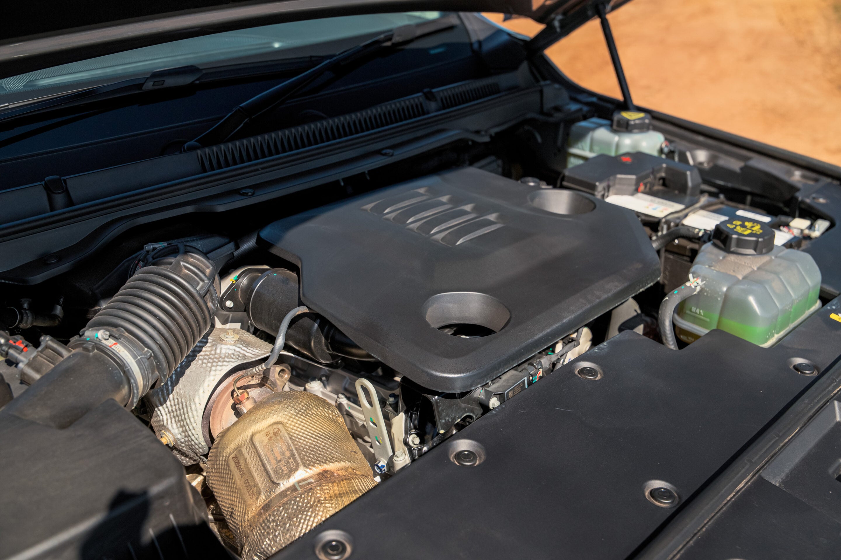Car engine bay with various components, including air intake hose, coolant reservoir, and battery visible under the hood.