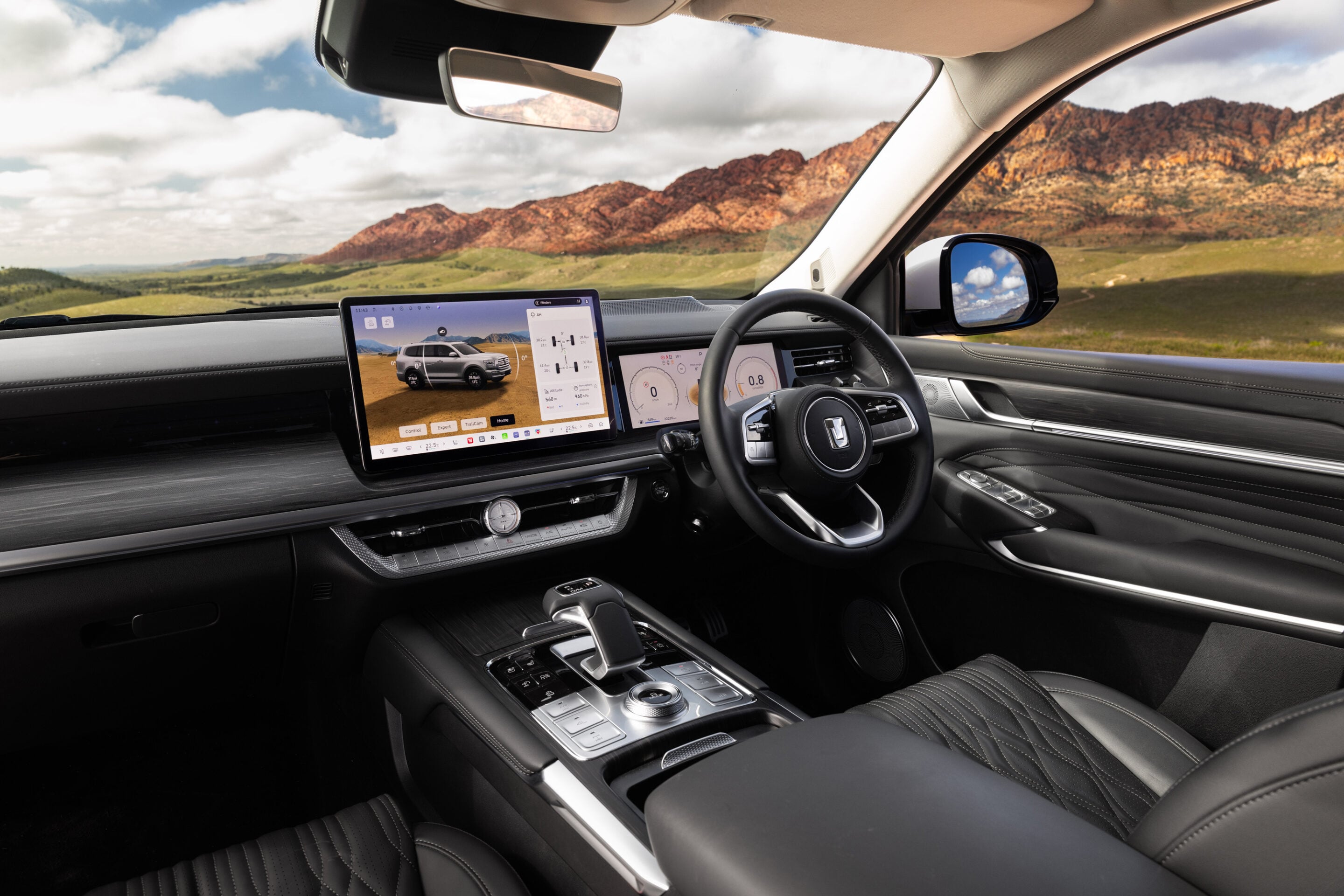 Luxurious SUV interior with large touchscreen displays and stitched leather seats, mountain landscape visible through windshield.