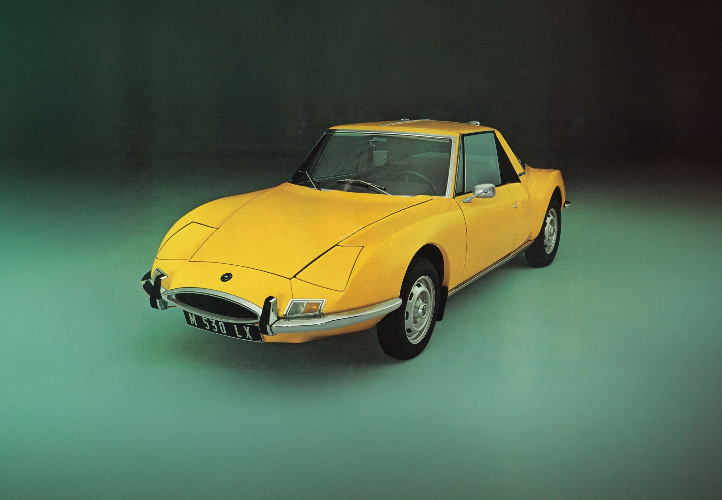 Front-left view of a yellow vintage sports car against a dark green gradient studio background.