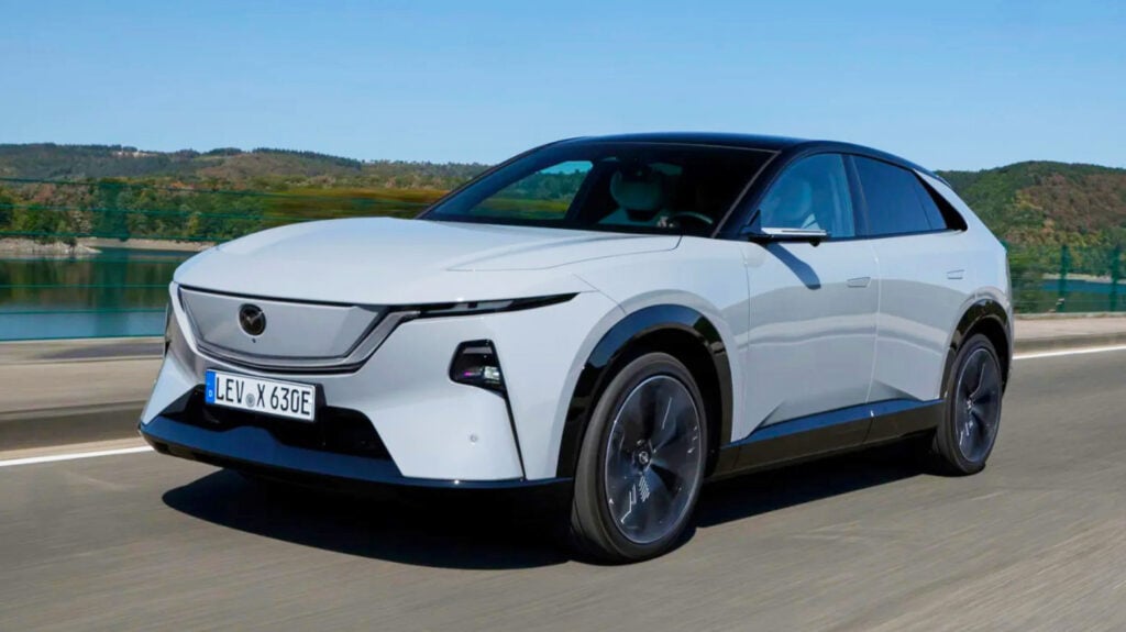 White electric car driving on a highway with blue sky and hills in the background.