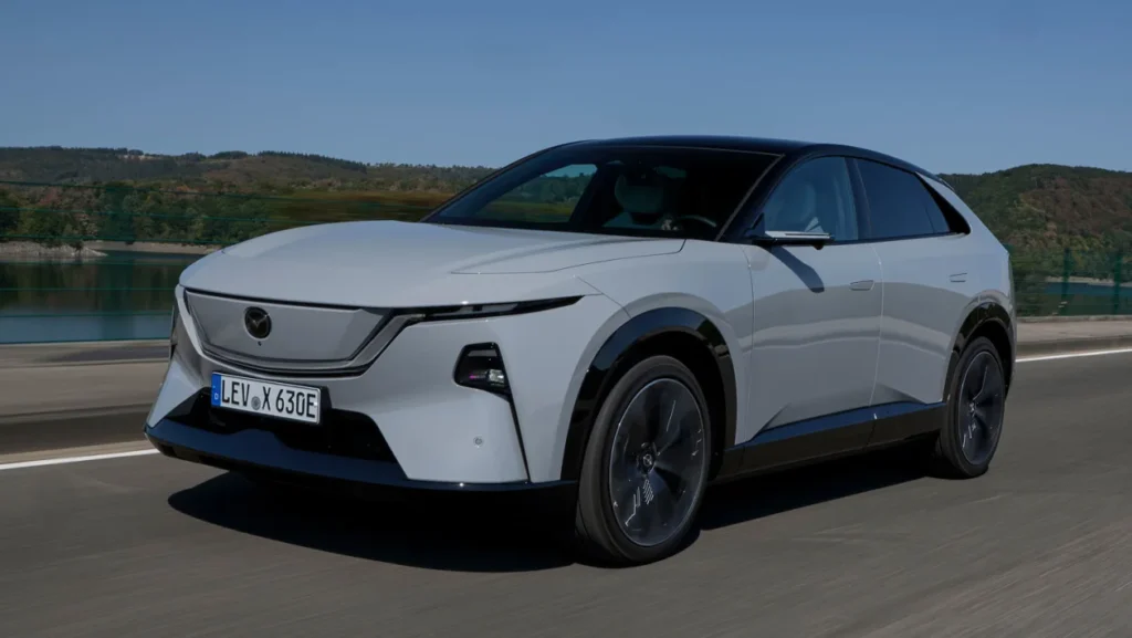 White electric crossover car driving on a highway with a scenic landscape in the background.
