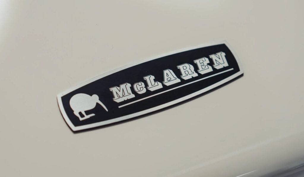 Close-up of a McLaren emblem on a light-colored car, with white text on a black plaque.