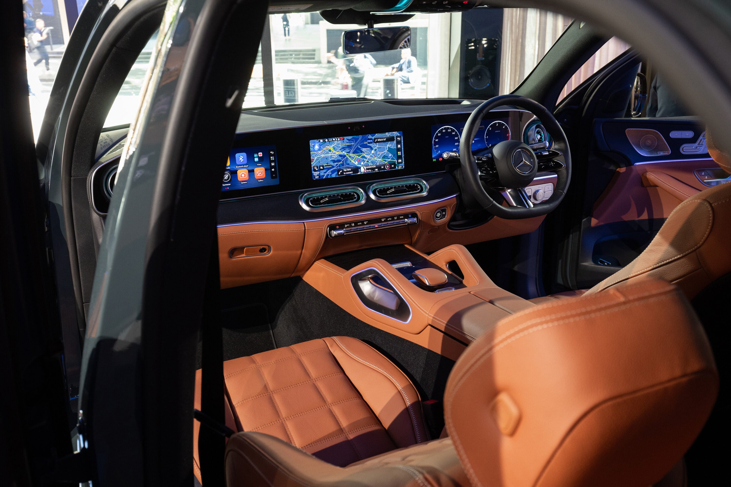 Interior of a luxury car with a wide digital dashboard, center touchscreen, and tan leather seats with stitching.