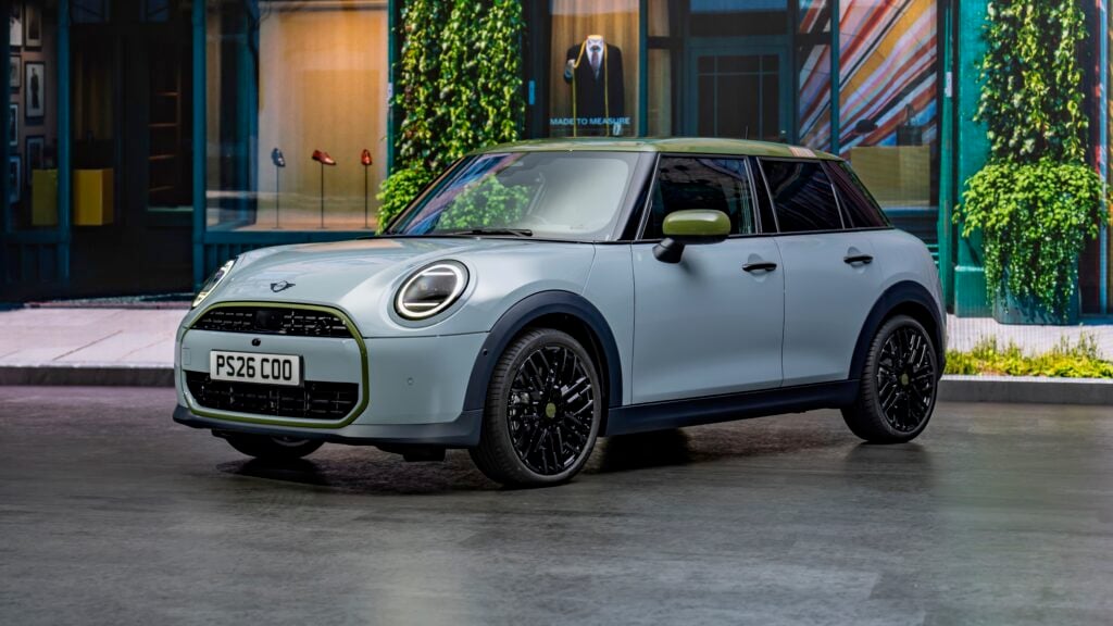 Silver Mini Cooper with lime-green trim parked on a city street in front of shop windows and ivy.