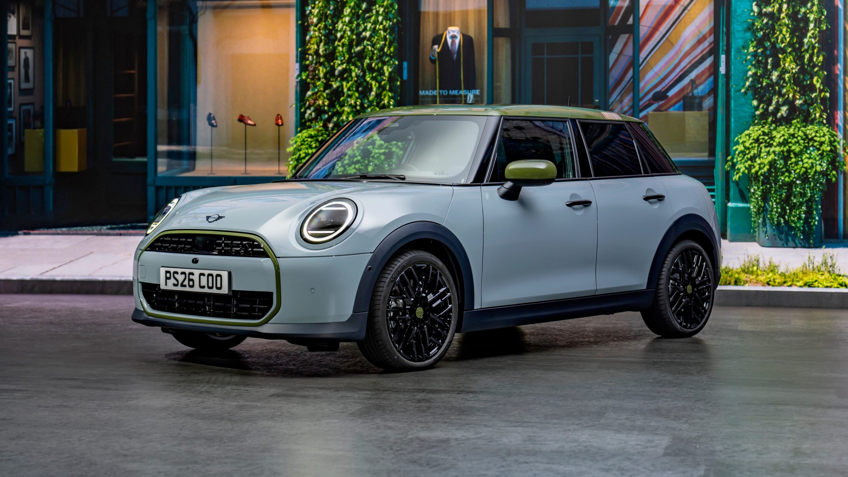 Silver Mini Cooper with lime-green trim parked on a city street in front of shop windows and ivy.
