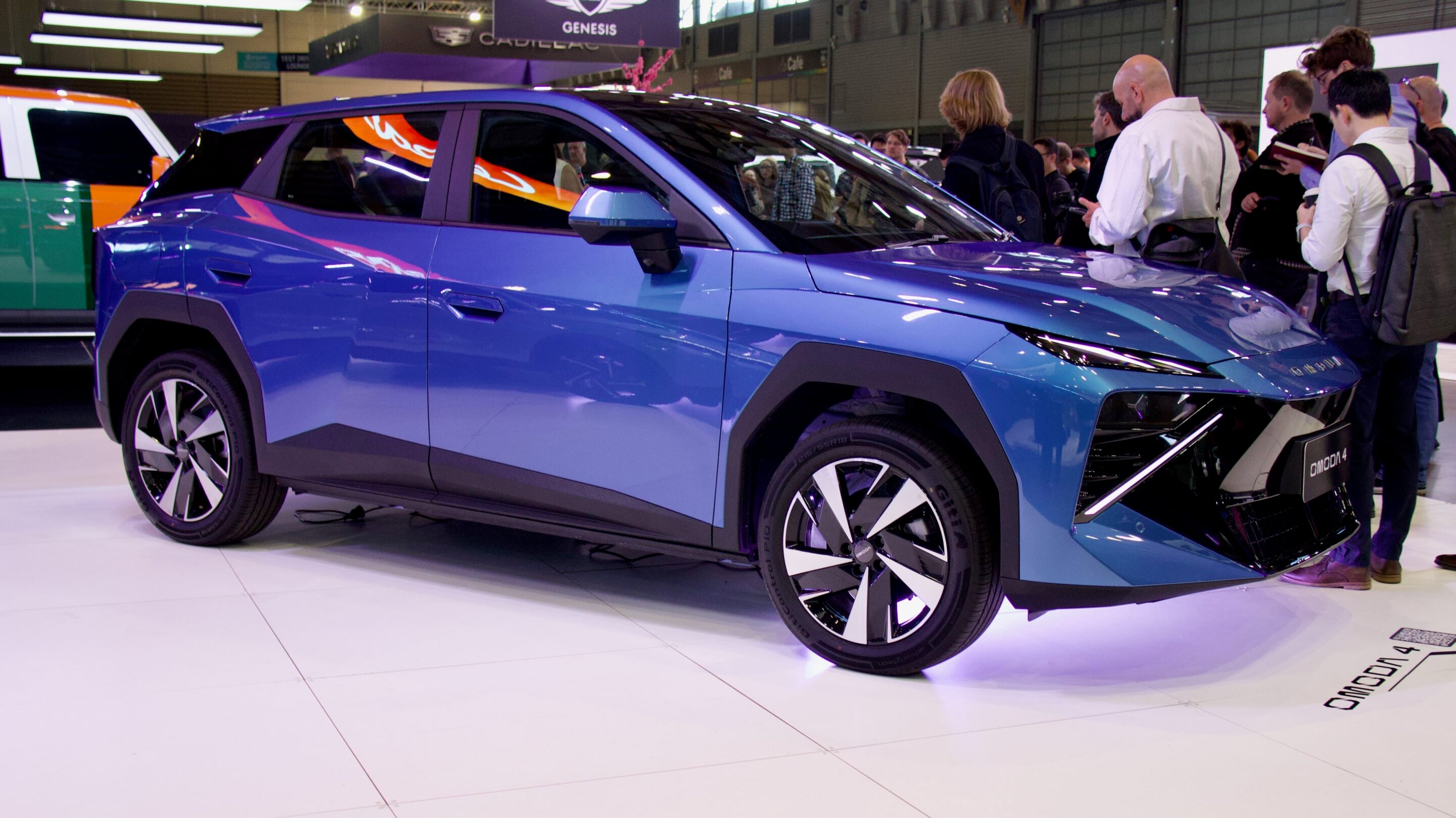 Blue SUV on display at a car show with people gathered around, admiring it in a bright exhibition hall.