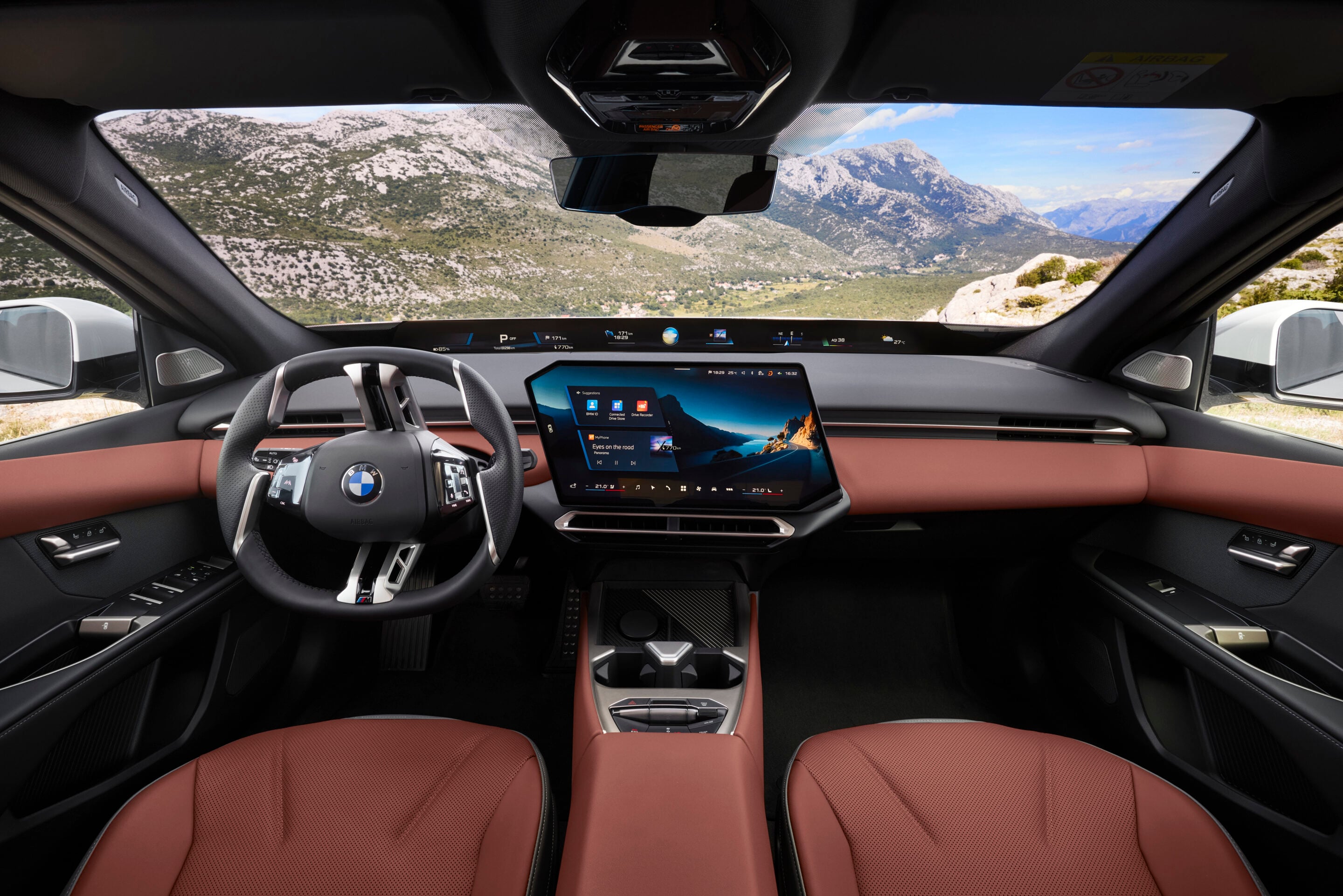 Luxury car interior with red leather seats, a large central touchscreen, and mountain scenery visible through the windshield.