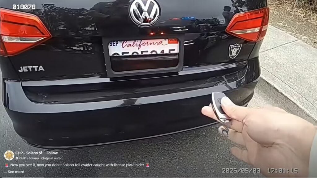 Rear view of a black Volkswagen Jetta with a California license plate; a hand holds a key fob in foreground, suggesting a car_unlock/remote access scene.