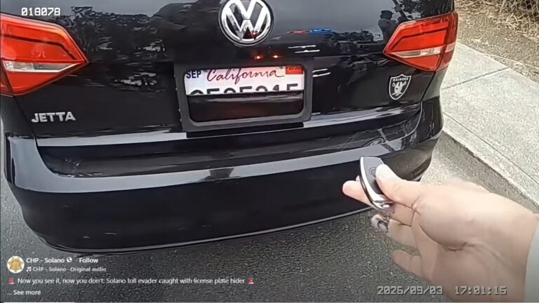 Rear view of a black Volkswagen Jetta with a California license plate; a hand holds a key fob in foreground, suggesting a car_unlock/remote access scene.