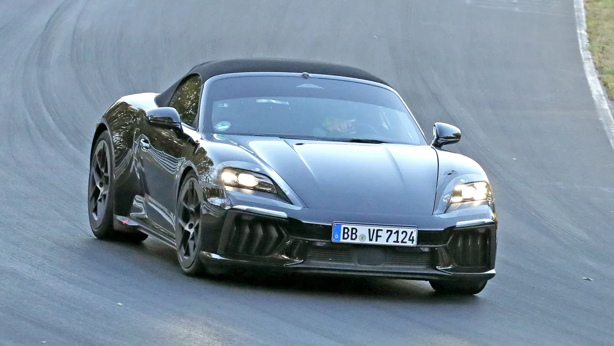 Gray convertible sports car on a racetrack taking a left-hand bend, headlights on.