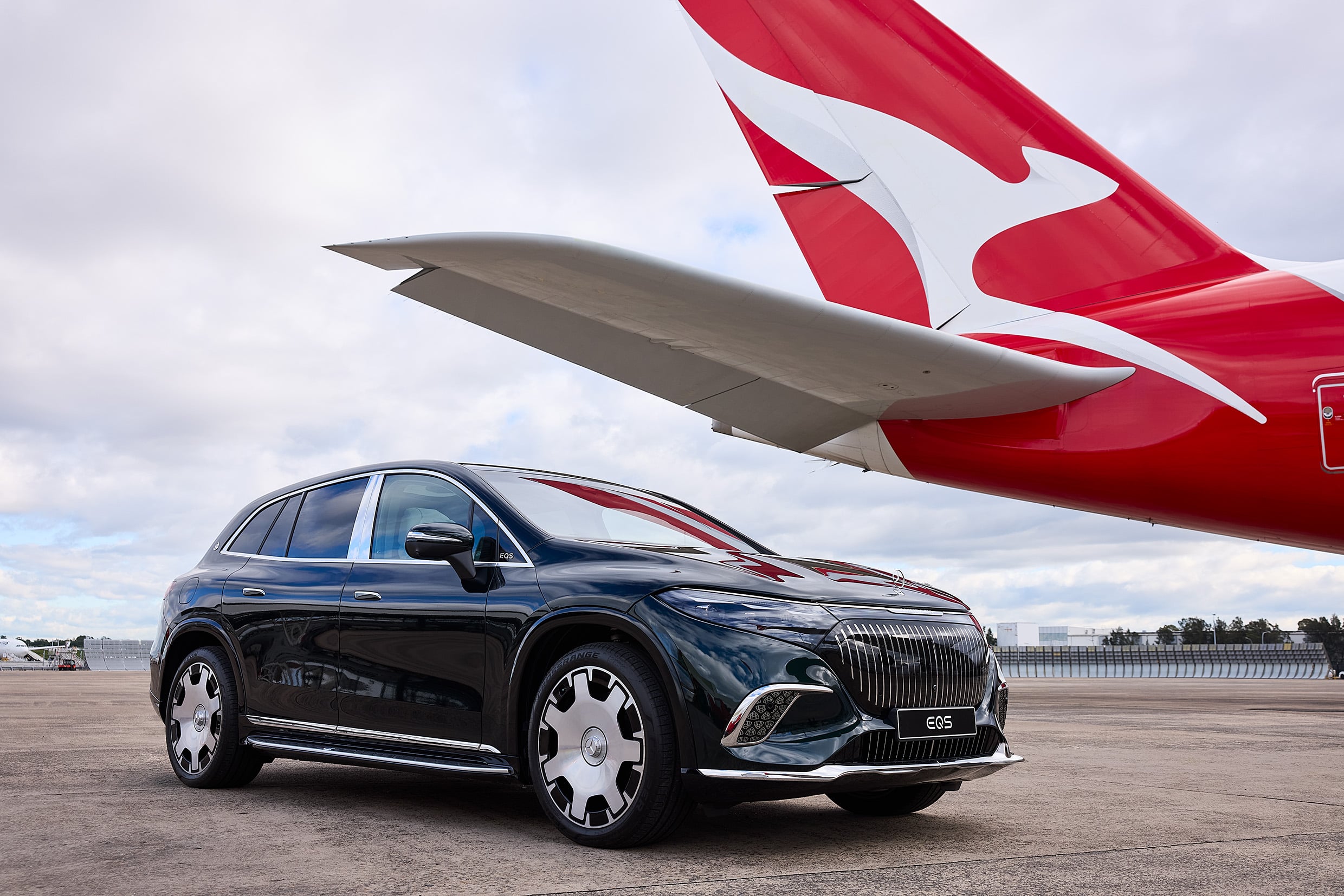 Black Mercedes‑Benz EQS SUV in the foreground on a tarmac with a red and white airplane tail visible in the background.