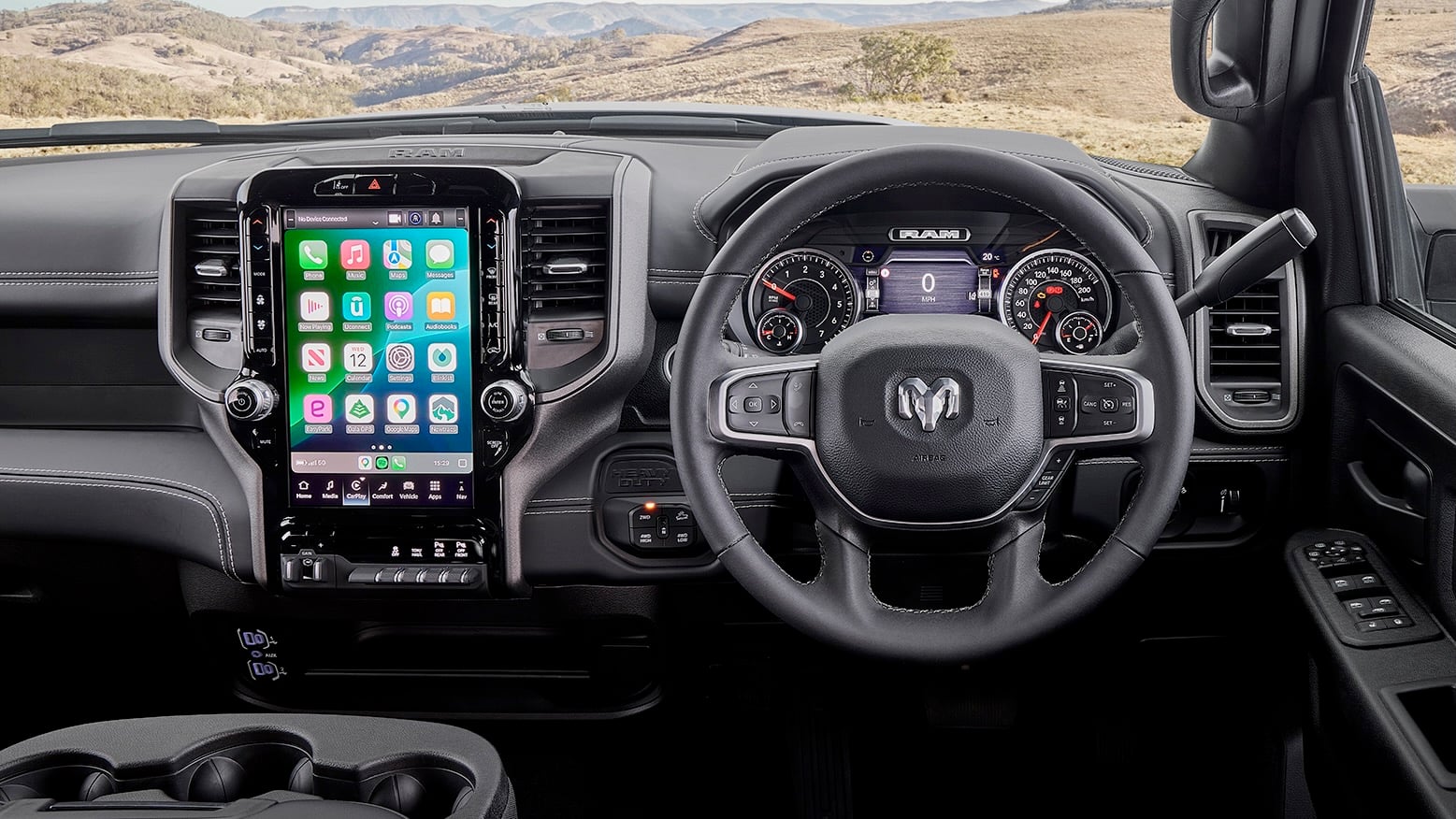 Interior of a RAM pickup showing a tall vertical touchscreen infotainment system, steering wheel, and digital instrument cluster with a desert landscape outside the windshield.