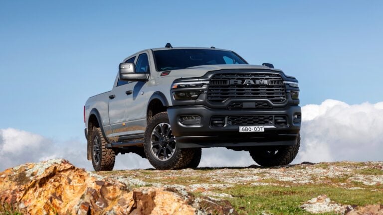 Grey RAM pickup truck parked on rocky terrain under a clear blue sky, front-facing view