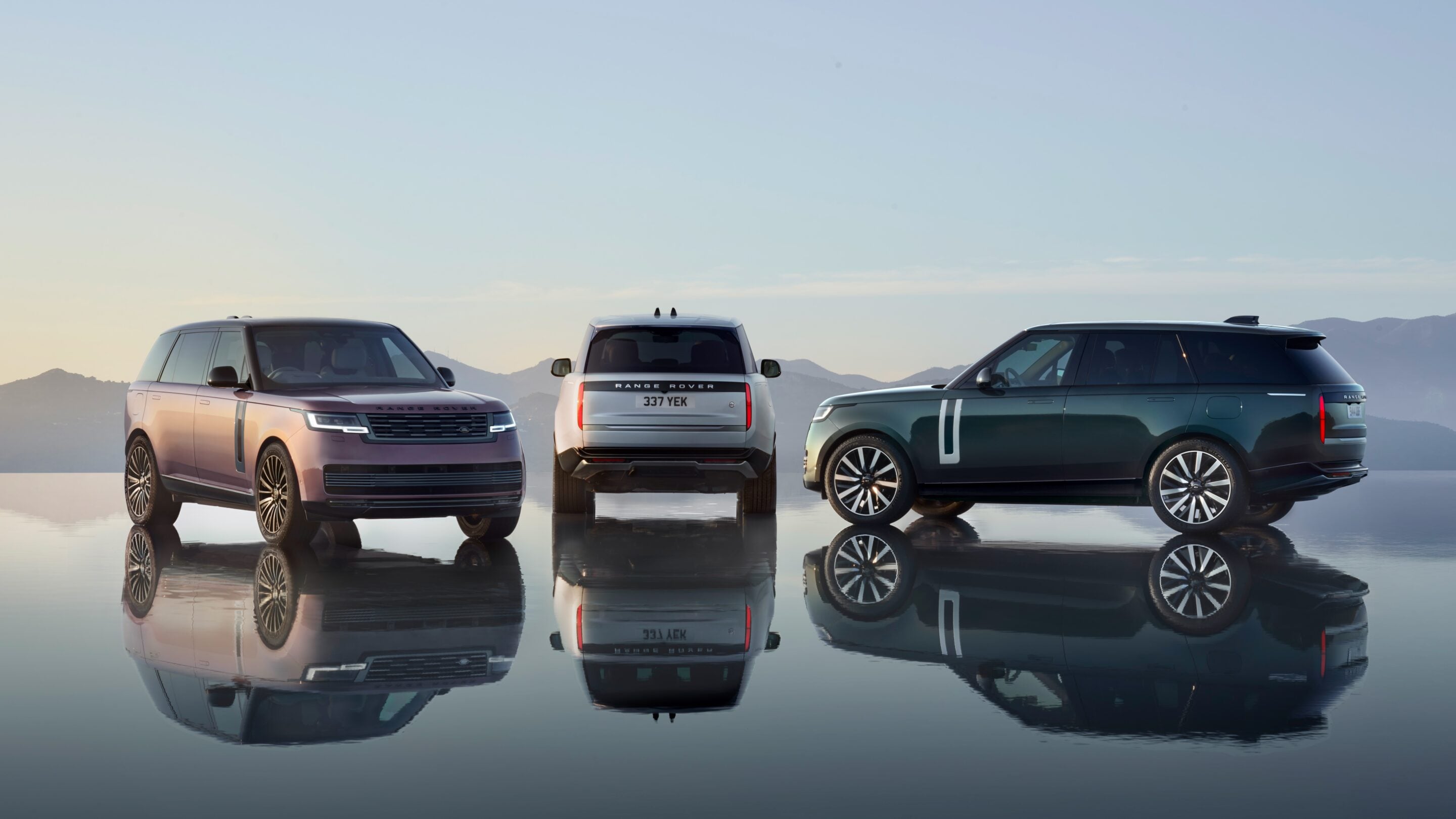 Three Range Rover SUVs parked on a reflective surface with mountains in the distance at sunset.