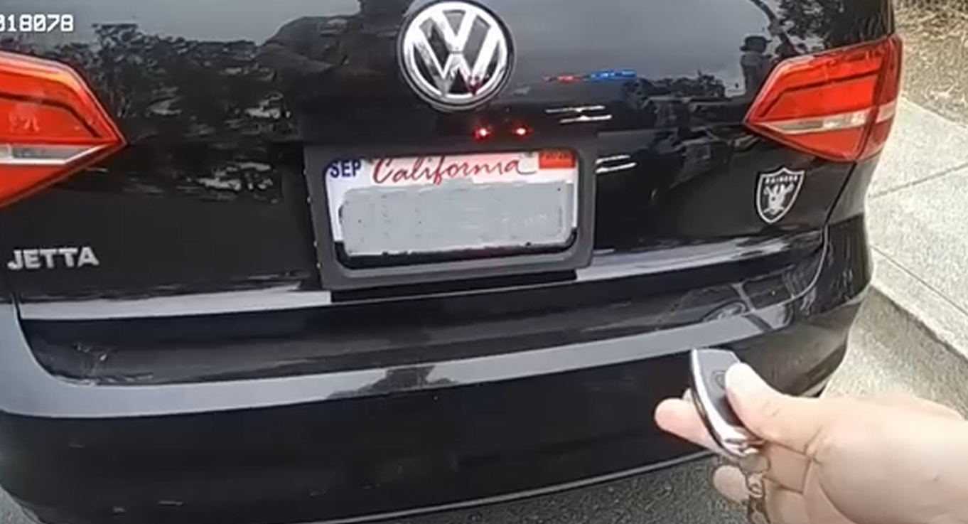 Rear view of a black VW Jetta with a California license plate; a hand holding a key fob is in the foreground near the trunk.