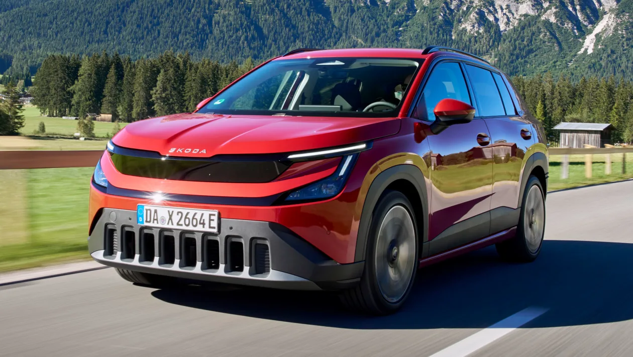 Red Skoda SUV driving on a rural road with green fields and mountains in the background,