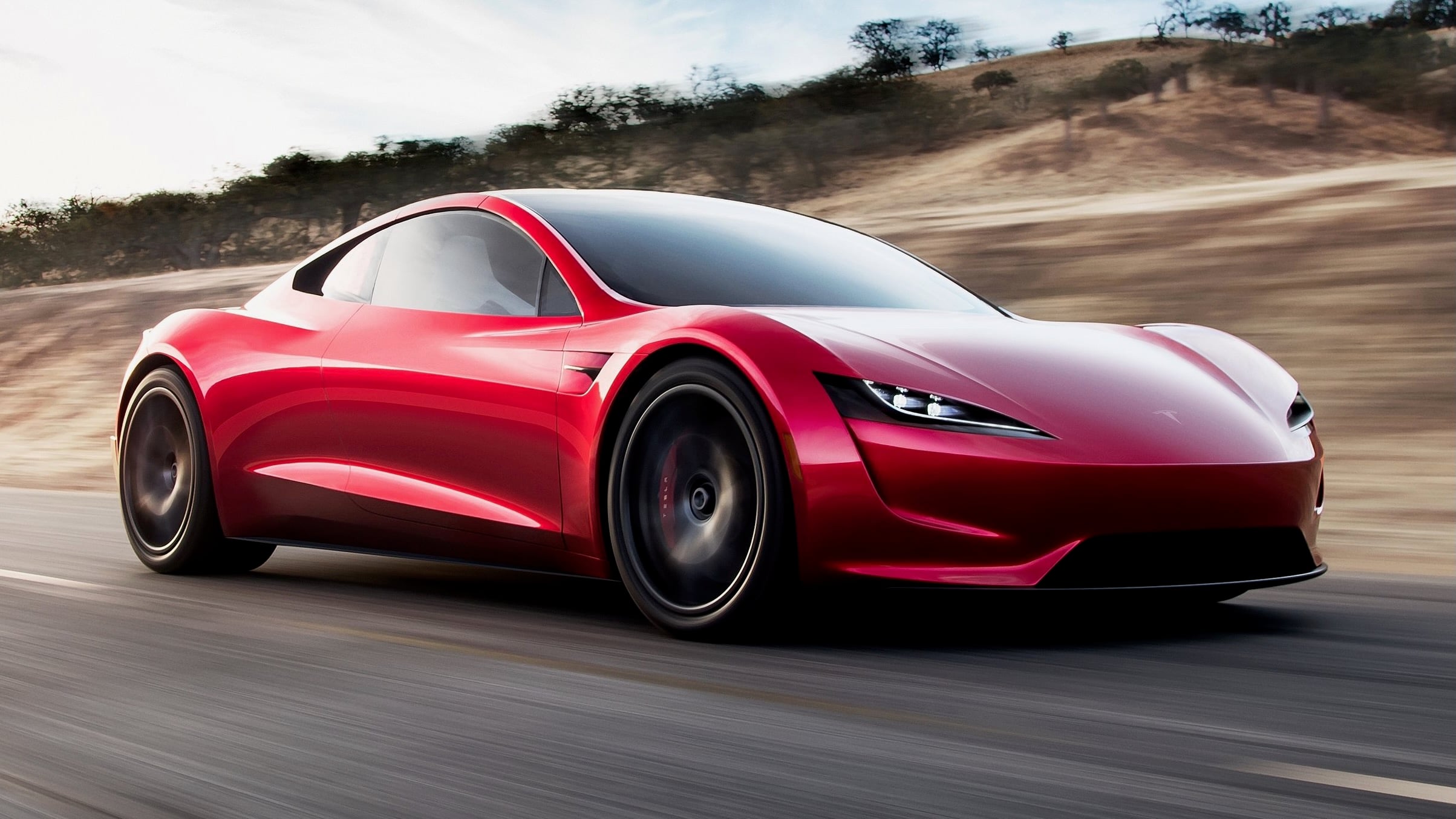 Red sports car speeding along a highway with a blurred desert hillside background, emphasizing sleek, aerodynamic styling.