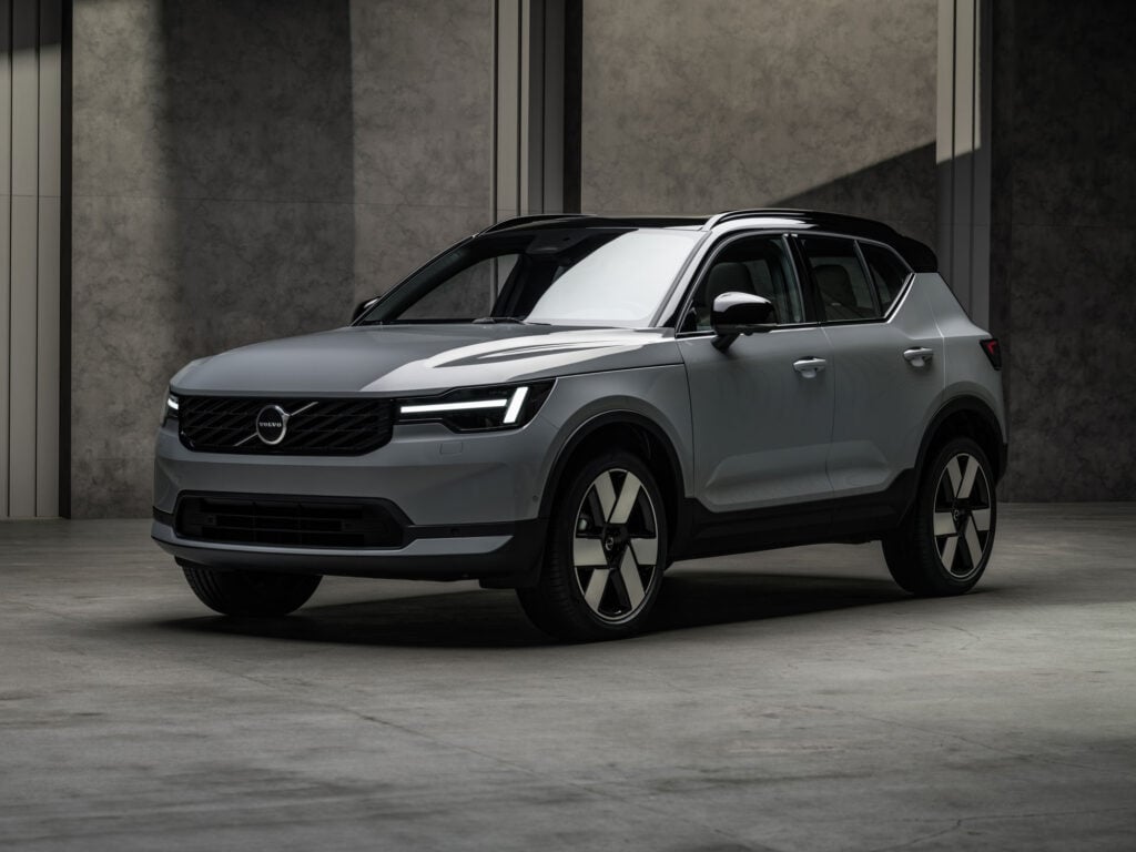 Front three-quarter view of a silver Volvo SUV in a dim, concrete-walled showroom, highlighting the grille and LED headlights in low light.