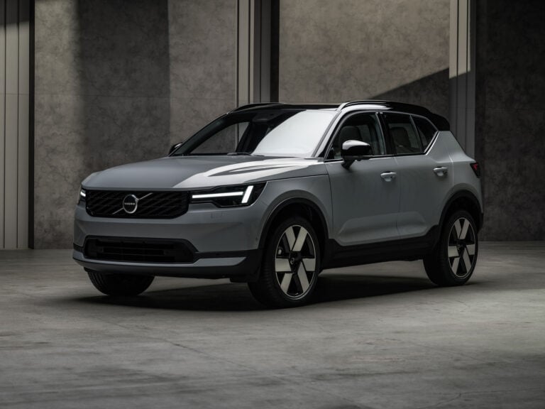 Front three-quarter view of a silver Volvo SUV in a dim, concrete-walled showroom, highlighting the grille and LED headlights in low light.
