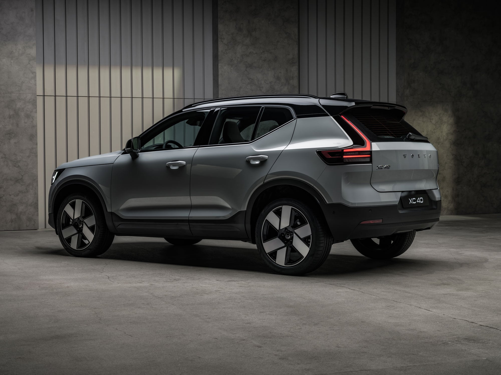 Silver Volvo XC40 SUV, rear three-quarter view in a dim, indoor setting against textured walls.
