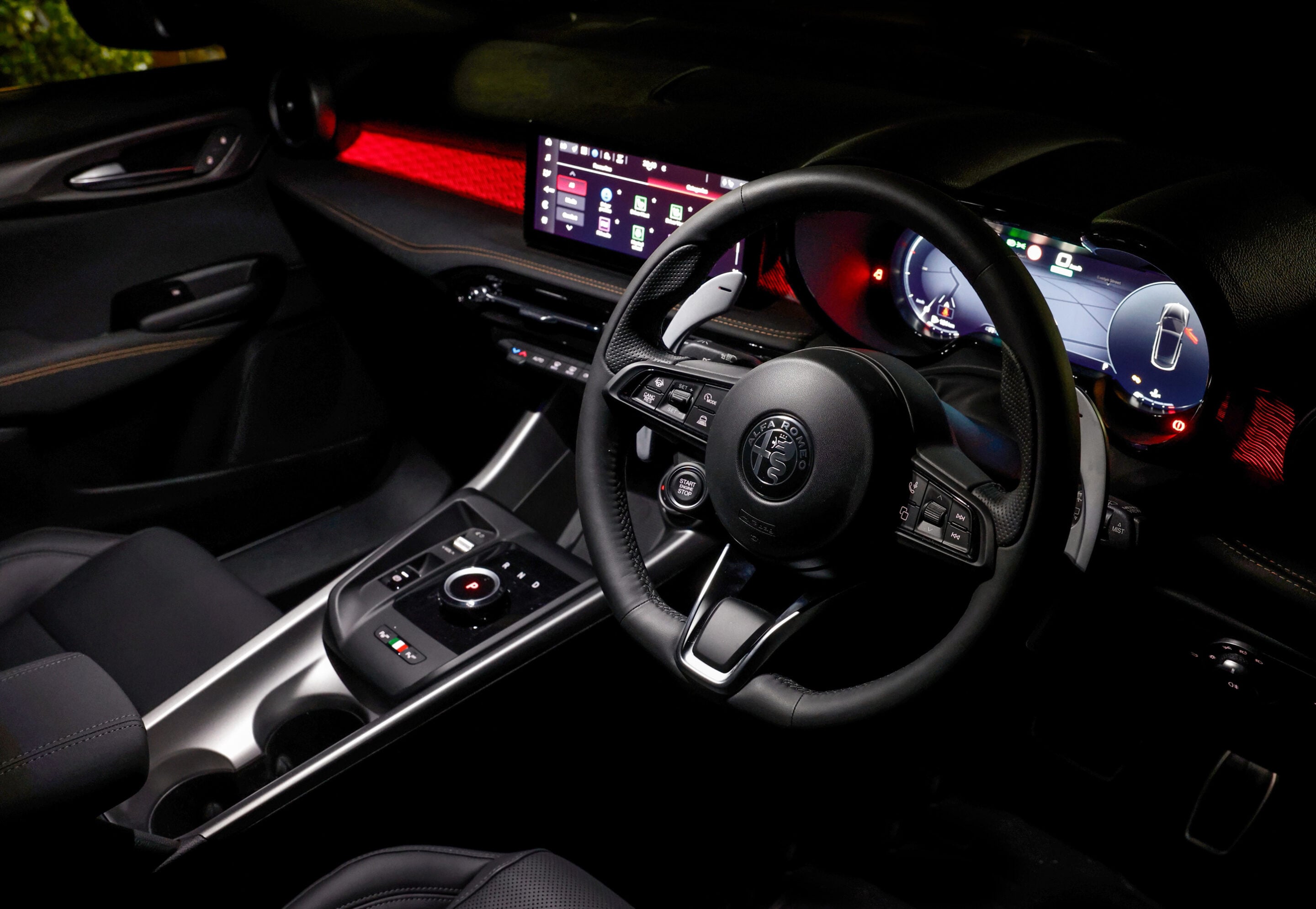 Interior of a luxury car cockpit at night with a digital instrument cluster and a wide touchscreen display.
