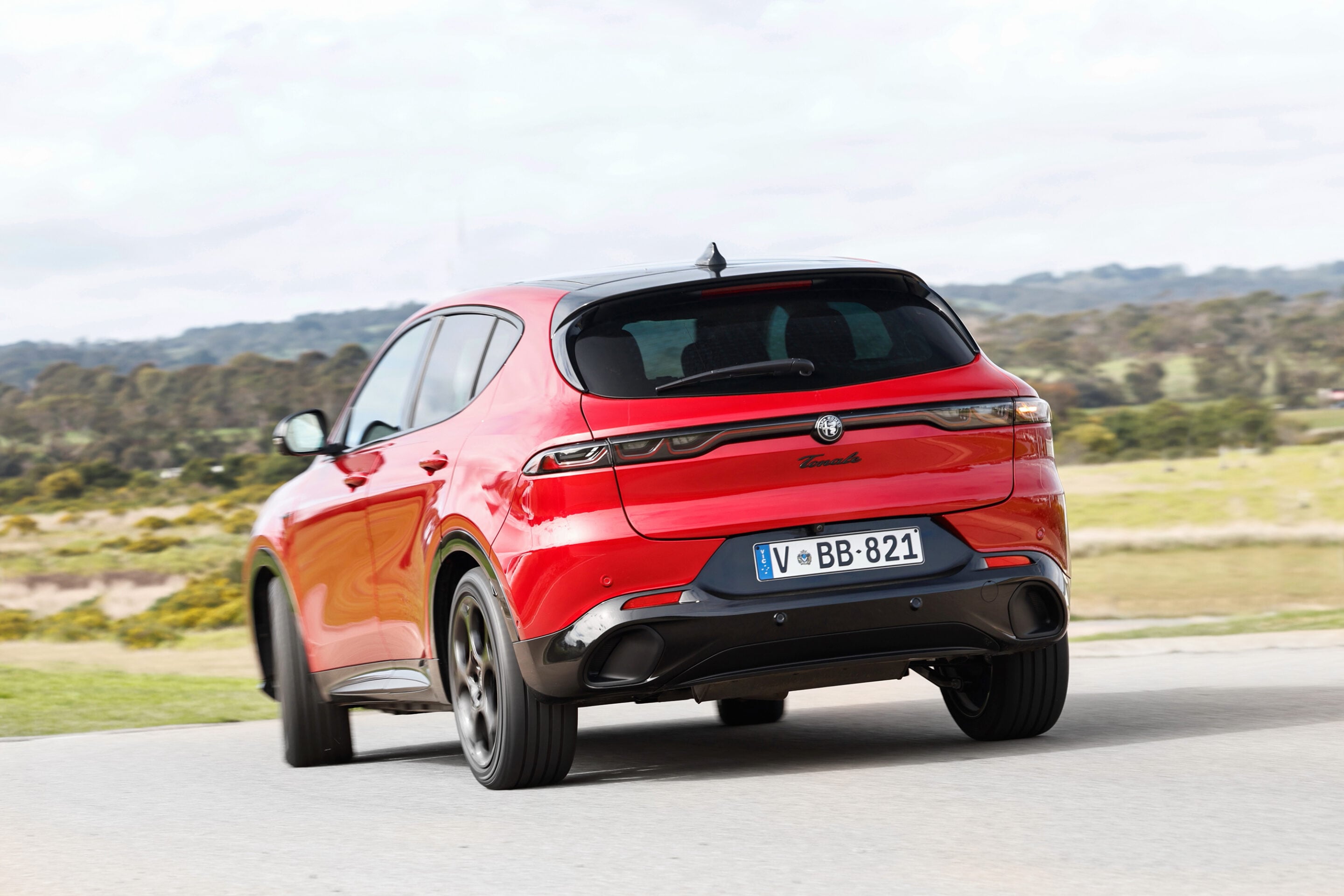 Red Alfa Romeo Tonale seen from the rear driving on a rural road, license plate V-BB-821, in motion.