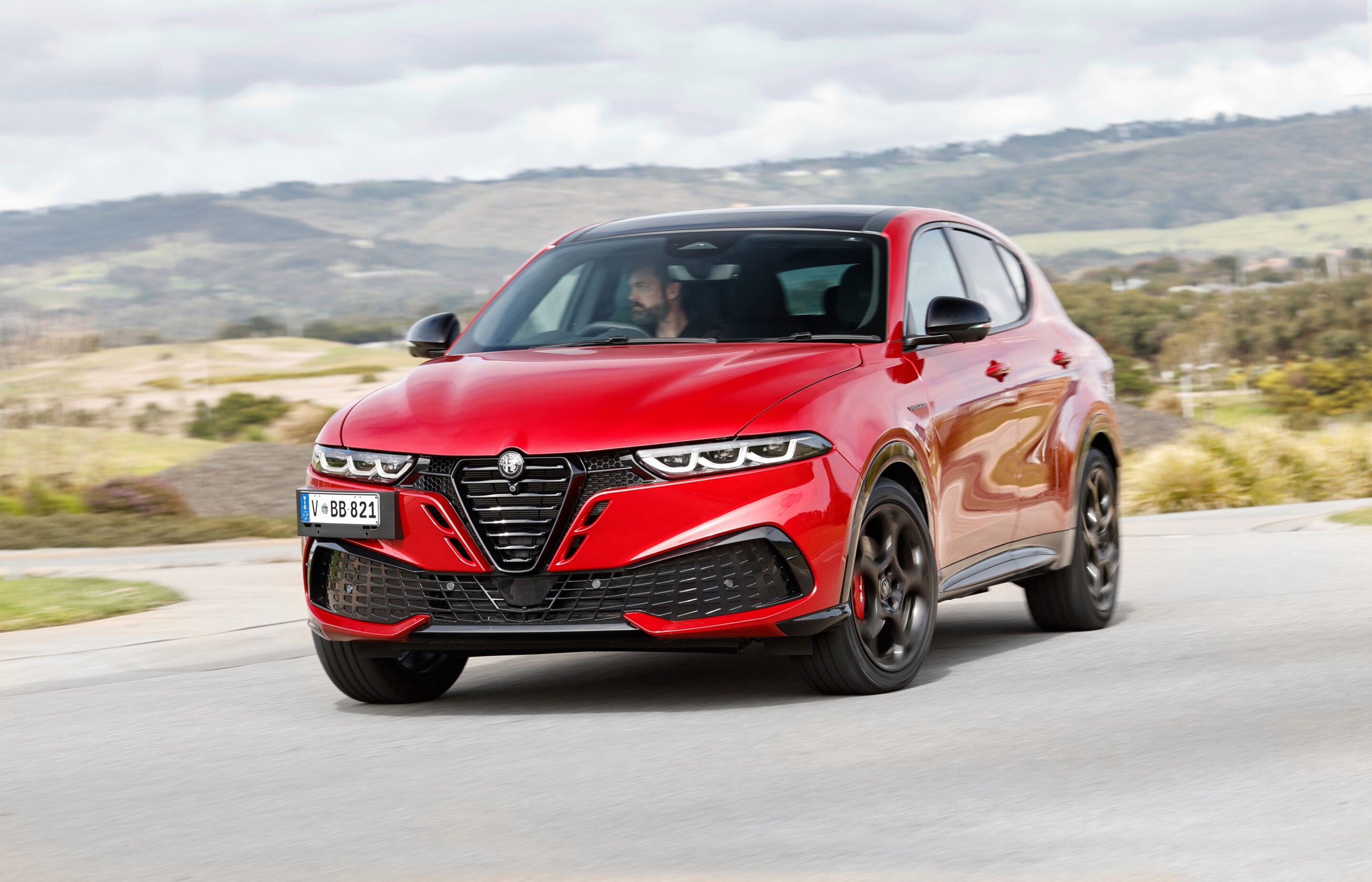 Red SUV driving along a curved road with hills in the distance, motion blurred background suggesting speed, front view