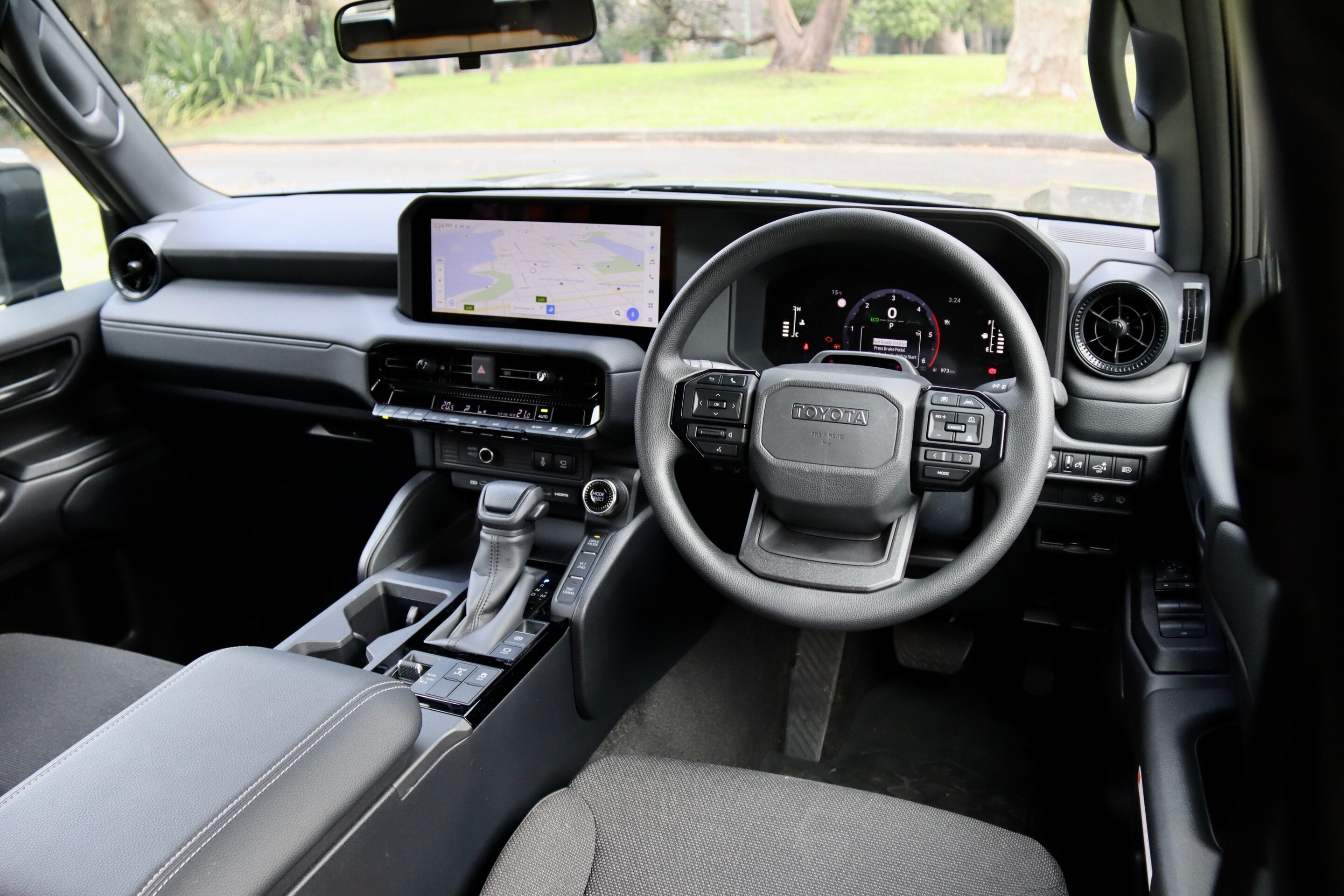 Interior of a modern vehicle showing a wide touchscreen infotainment system and digital gauge cluster behind the steering wheel behind-center console gear shifter visible