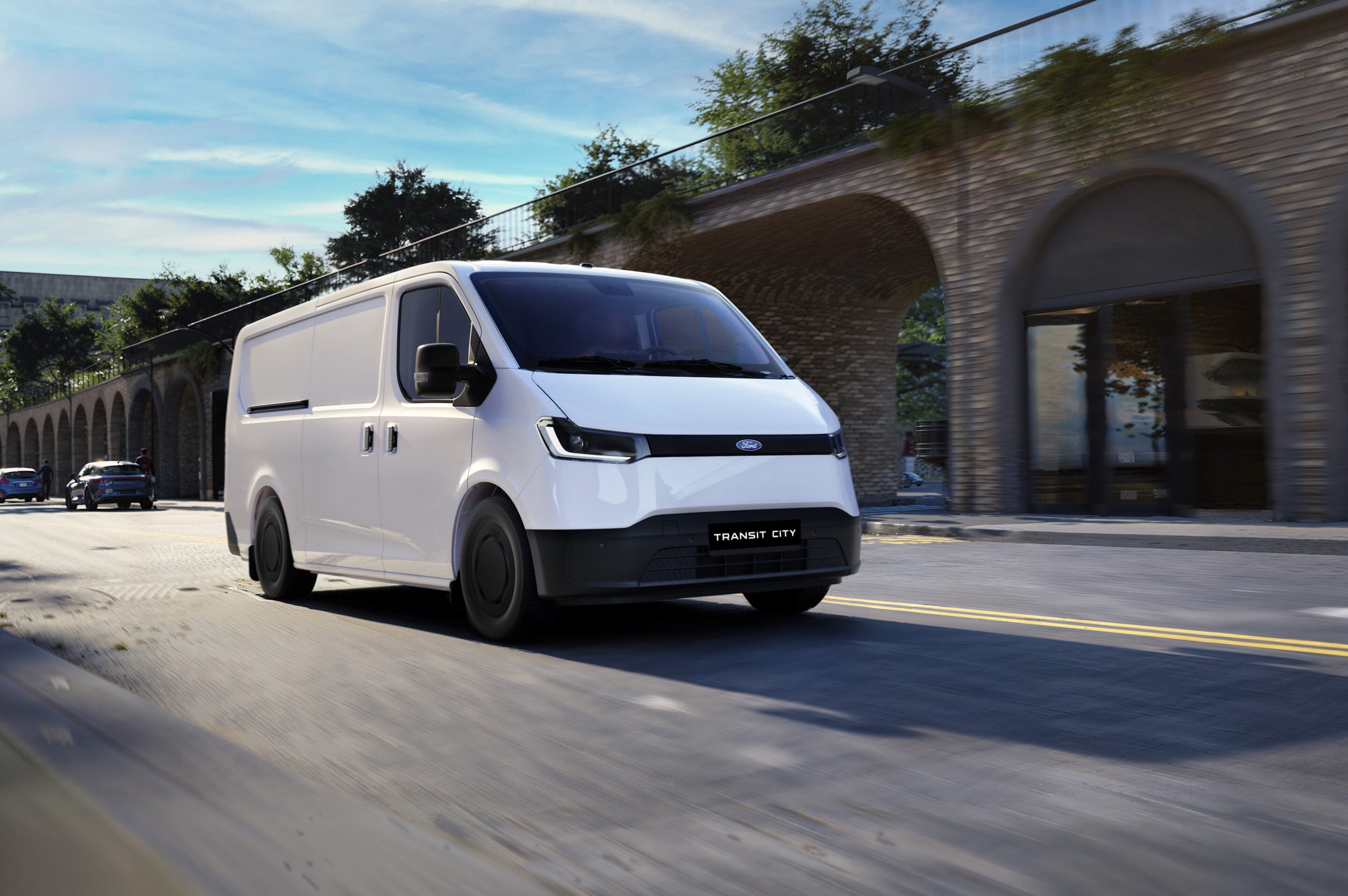 White Ford Transit City van driving along a street under a brick-arched viaduct on a sunny day