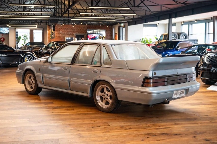 Silver four-door sedan on display inside a car dealership showroom with other vehicles in the background.