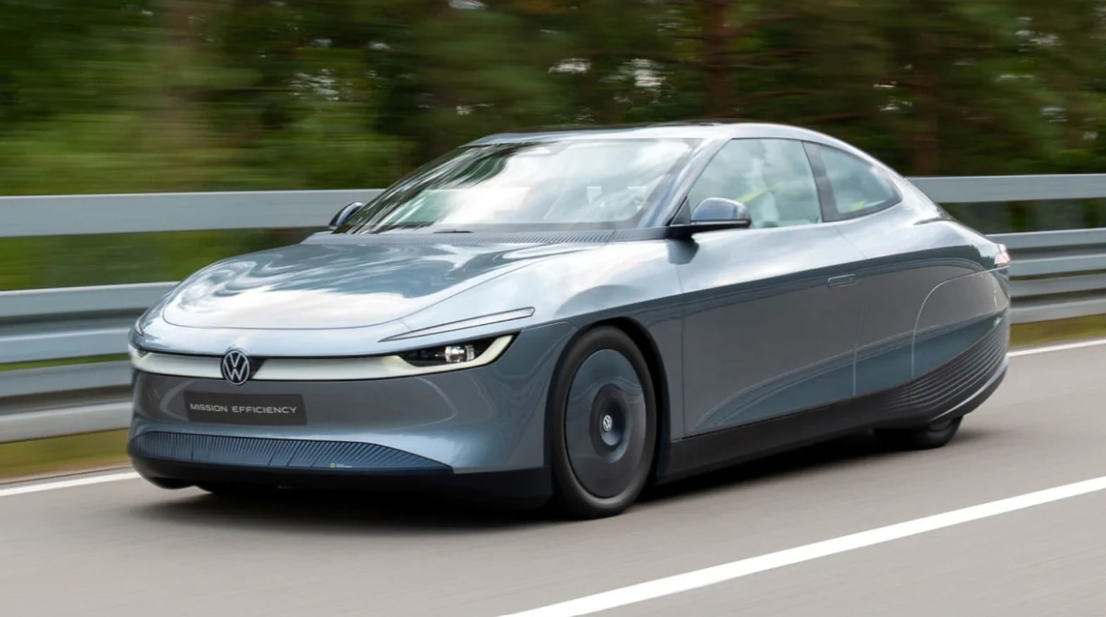 Gray Volkswagen concept car labeled 'Mission Efficiency' driving on a highway with guardrails in motion blur.