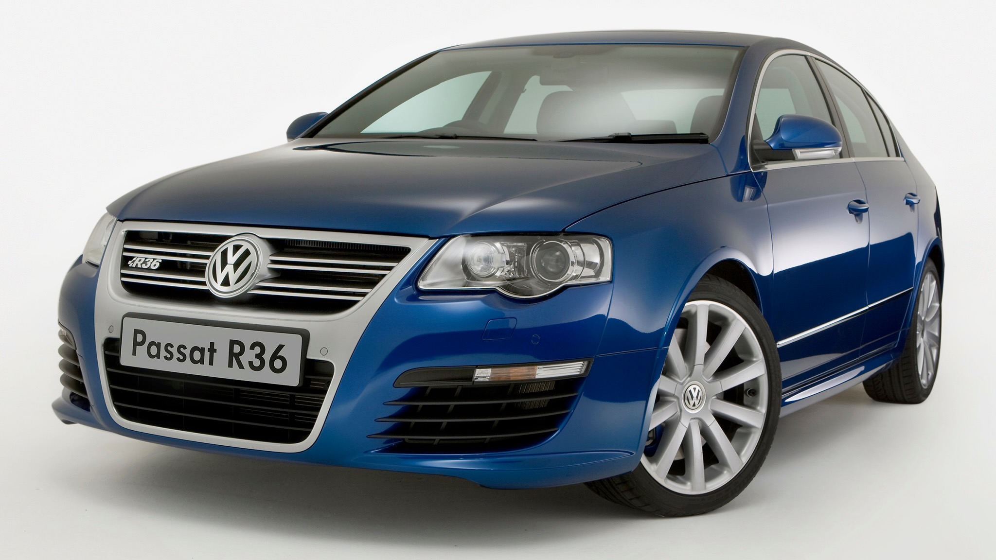 Front three-quarter view of a blue Volkswagen Passat R36, highlighting the grille, headlight, and alloy wheel behind the door. It reads 'Passat R36' on the plate.