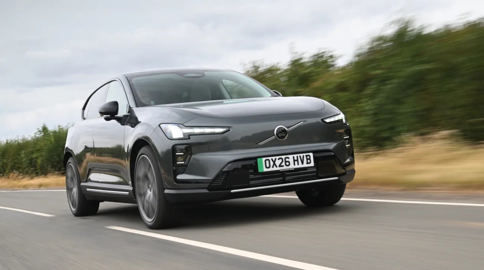 Gray Volvo SUV driving on a highway, front three-quarter view with blurred countryside in the background