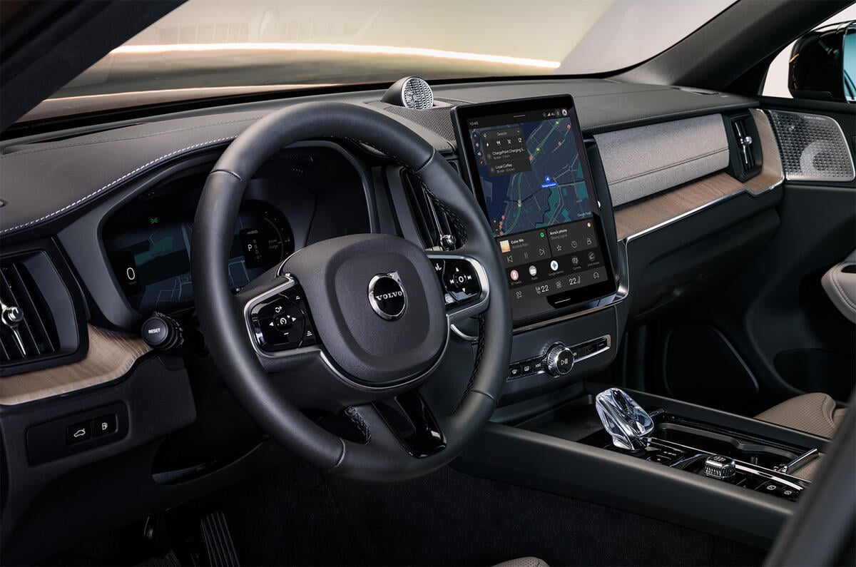 Volvo car interior with a tall touchscreen navigation screen, steering wheel, and wood trim dashboard