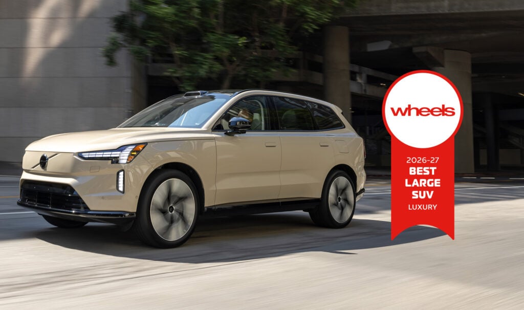 Beige luxury SUV driving on an urban street with a large red Wheels award badge on the right side.