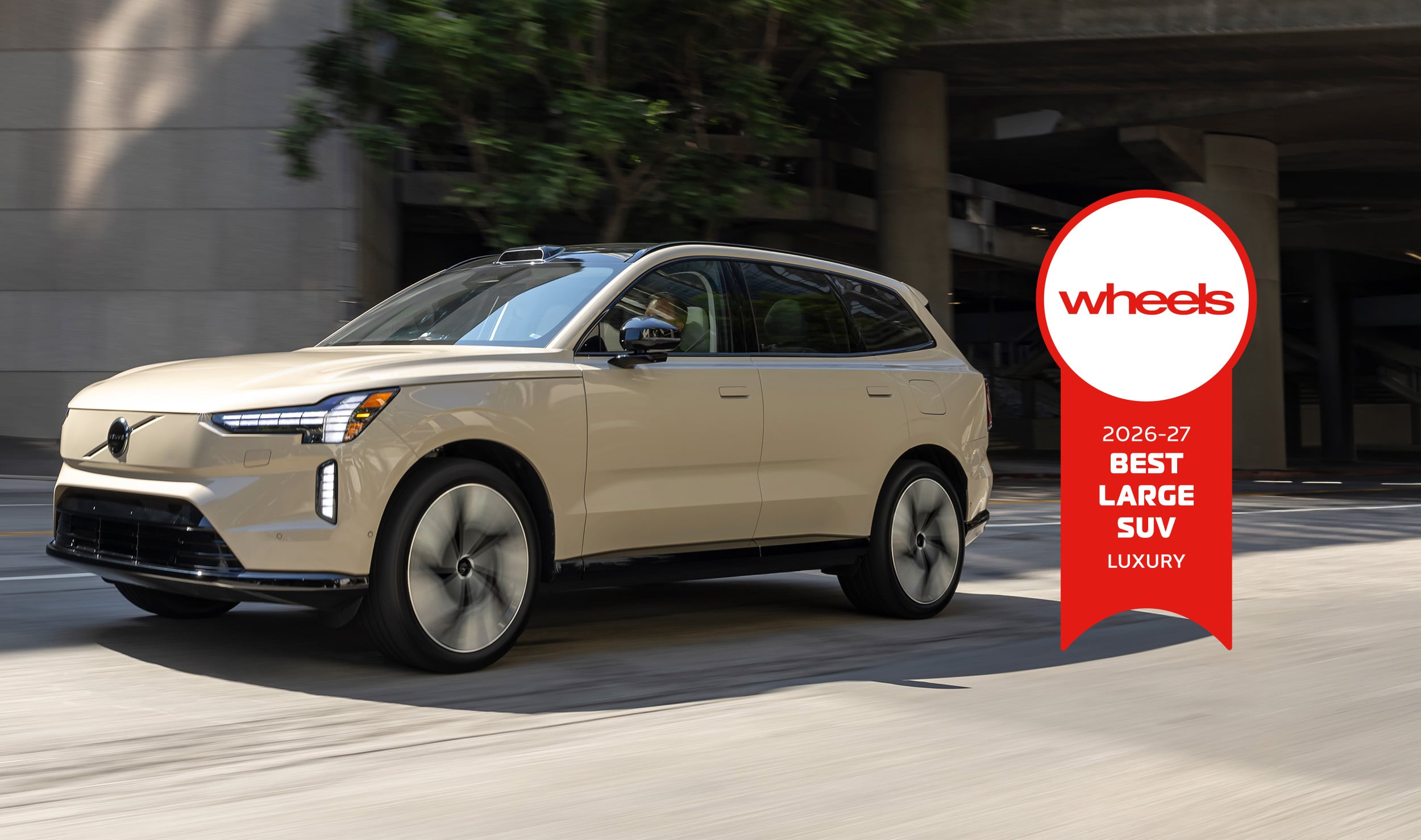 Beige luxury SUV driving on an urban street with a large red Wheels award badge on the right side.