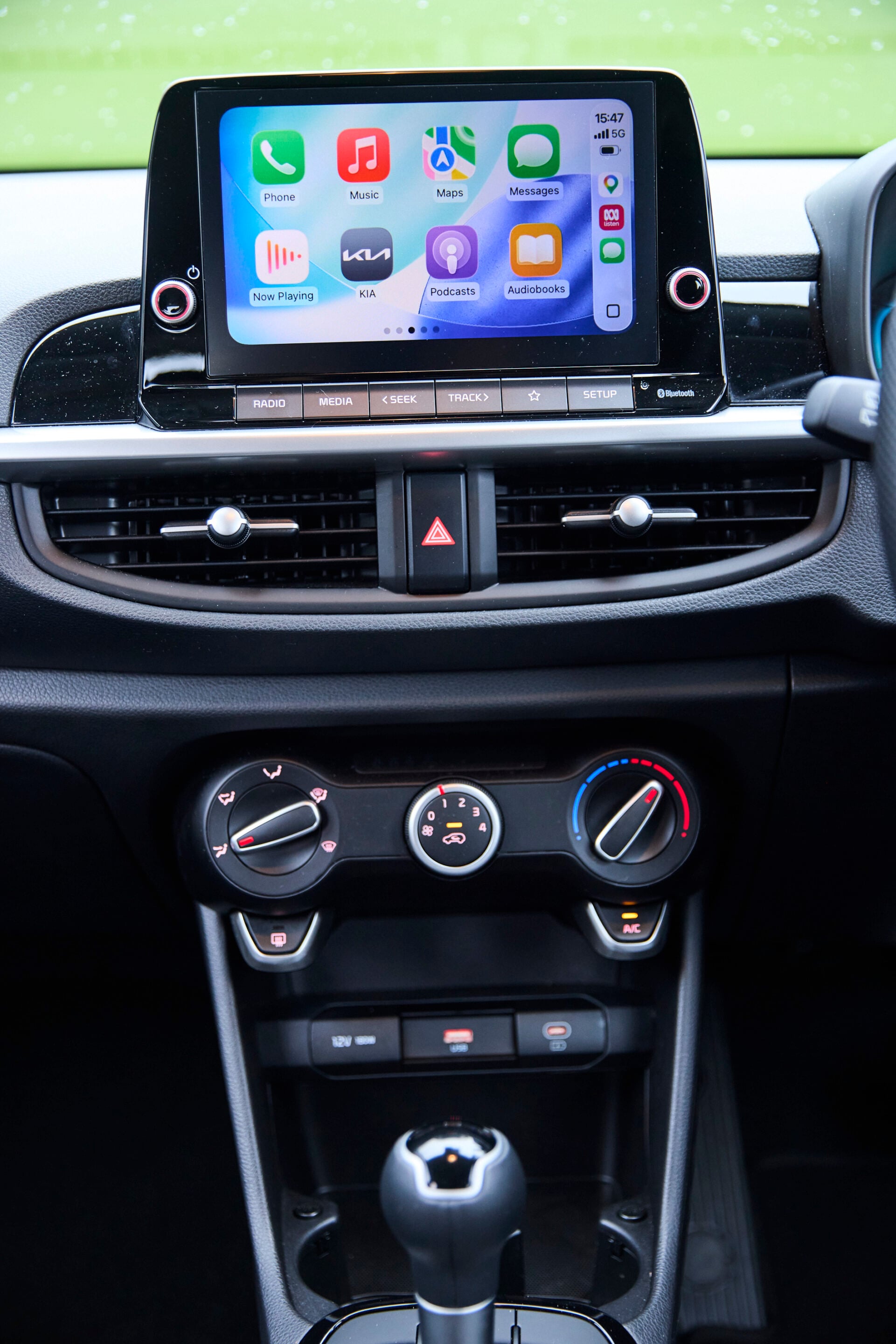 Car dashboard with a large touchscreen showing app icons; climate controls and gear shifter in view.