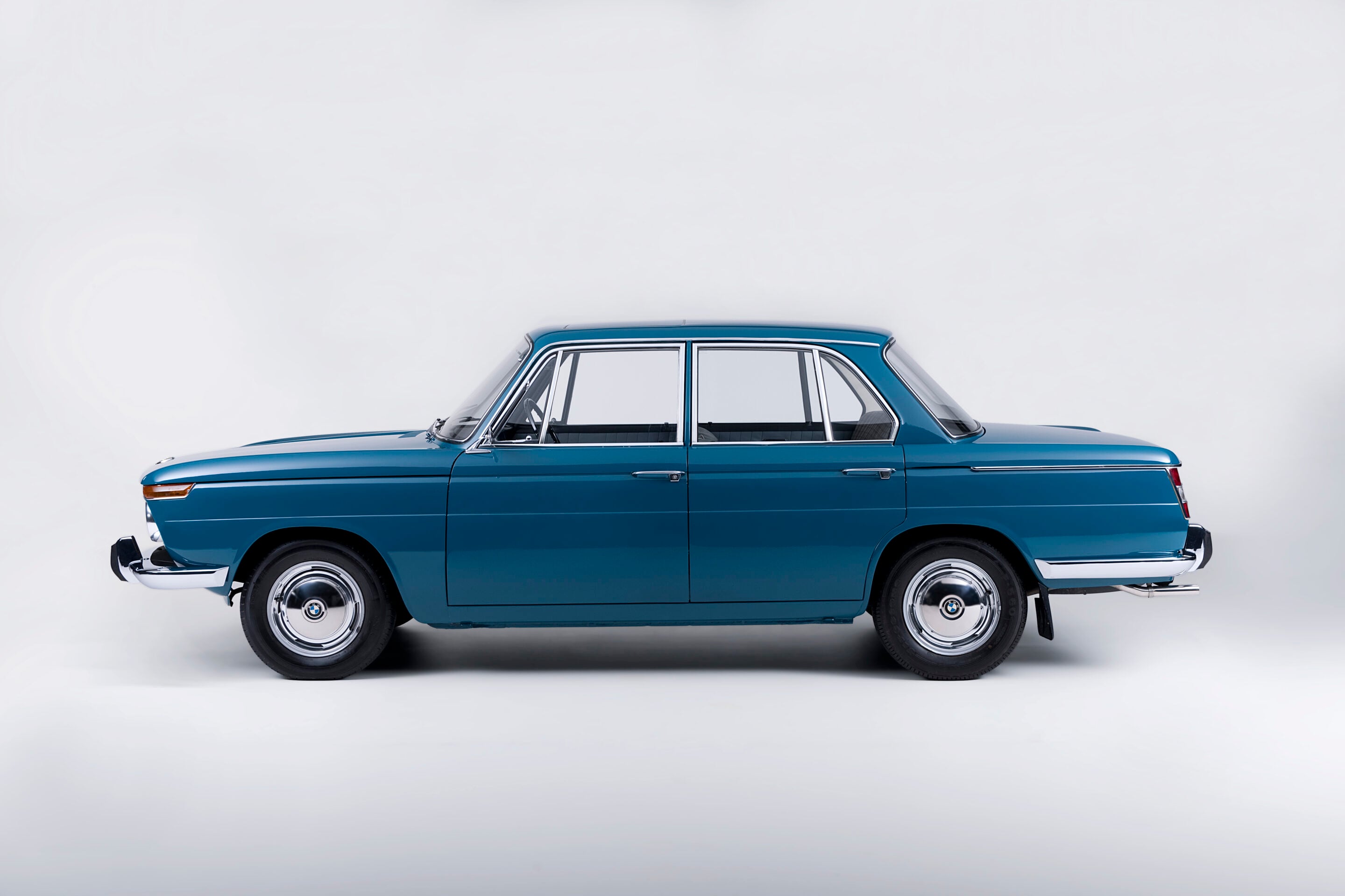 Side view of a blue vintage sedan with chrome trim photographed in a white studio backdrop, wheels visible on both ends.