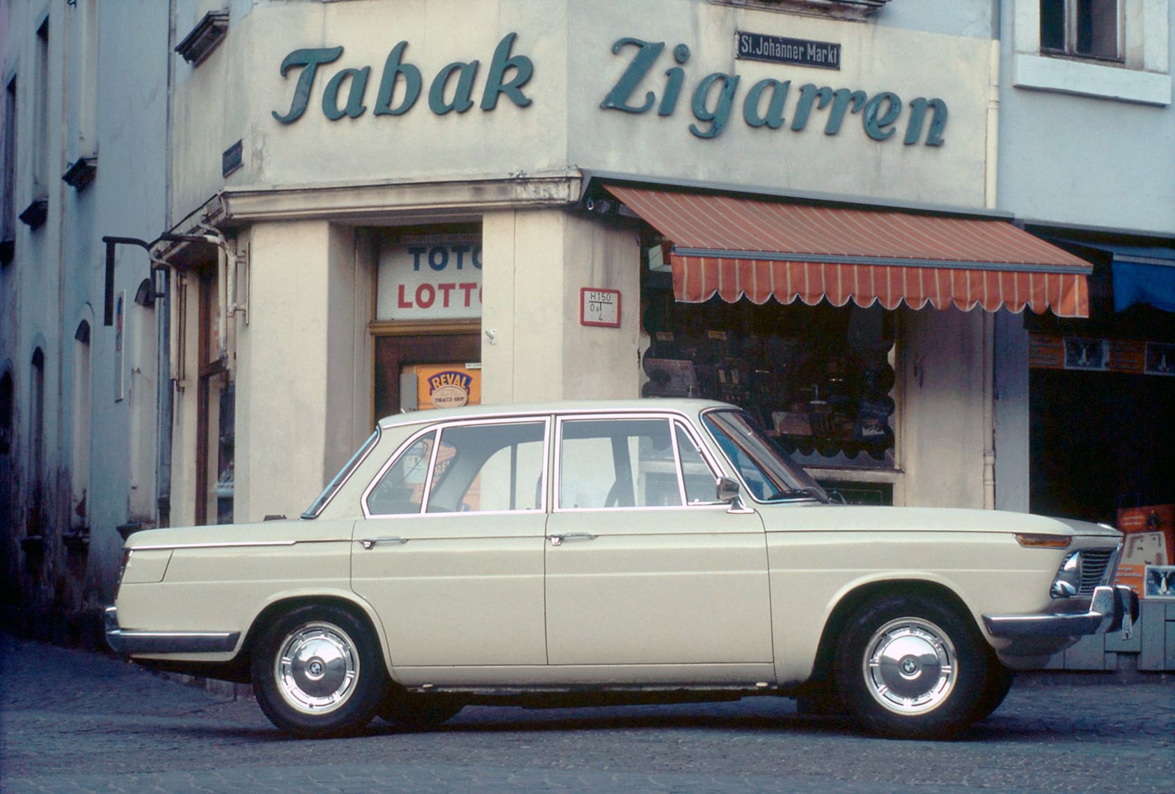 Vintage car parked in front of a tobacco shop with a 'Tabak Zigarren' sign on the building facade.