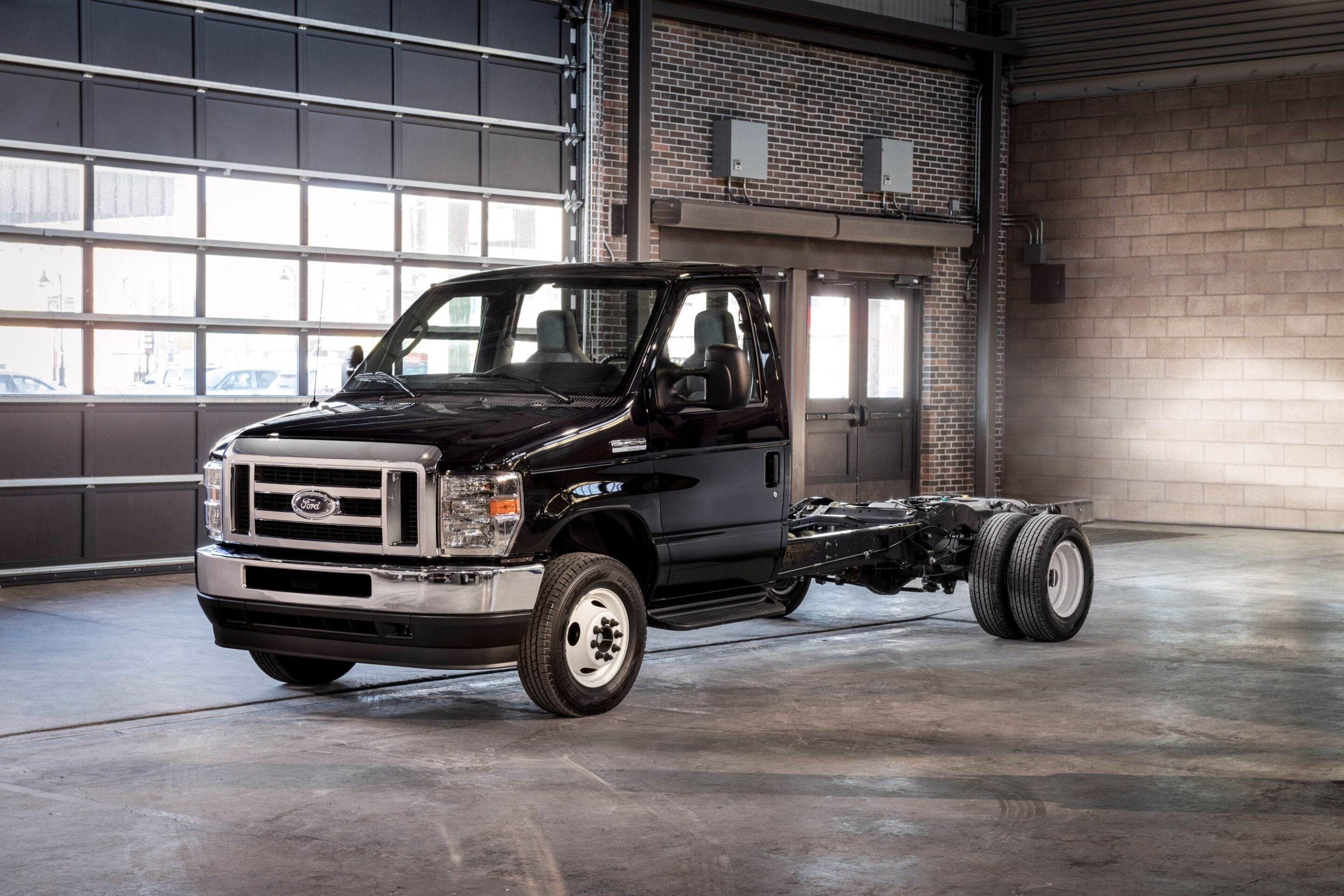 Black Ford pickup truck in a brick-walled auto shop, front cab and exposed chassis visible near a large garage door.