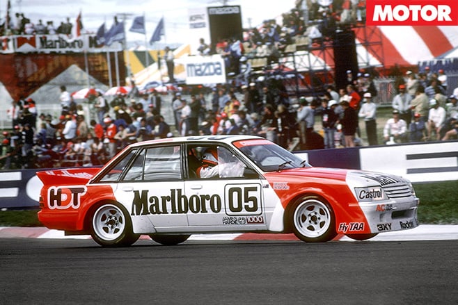 Red and white race car with Marlboro 05 livery speeding along a track, grandstands filled with spectators in the background.